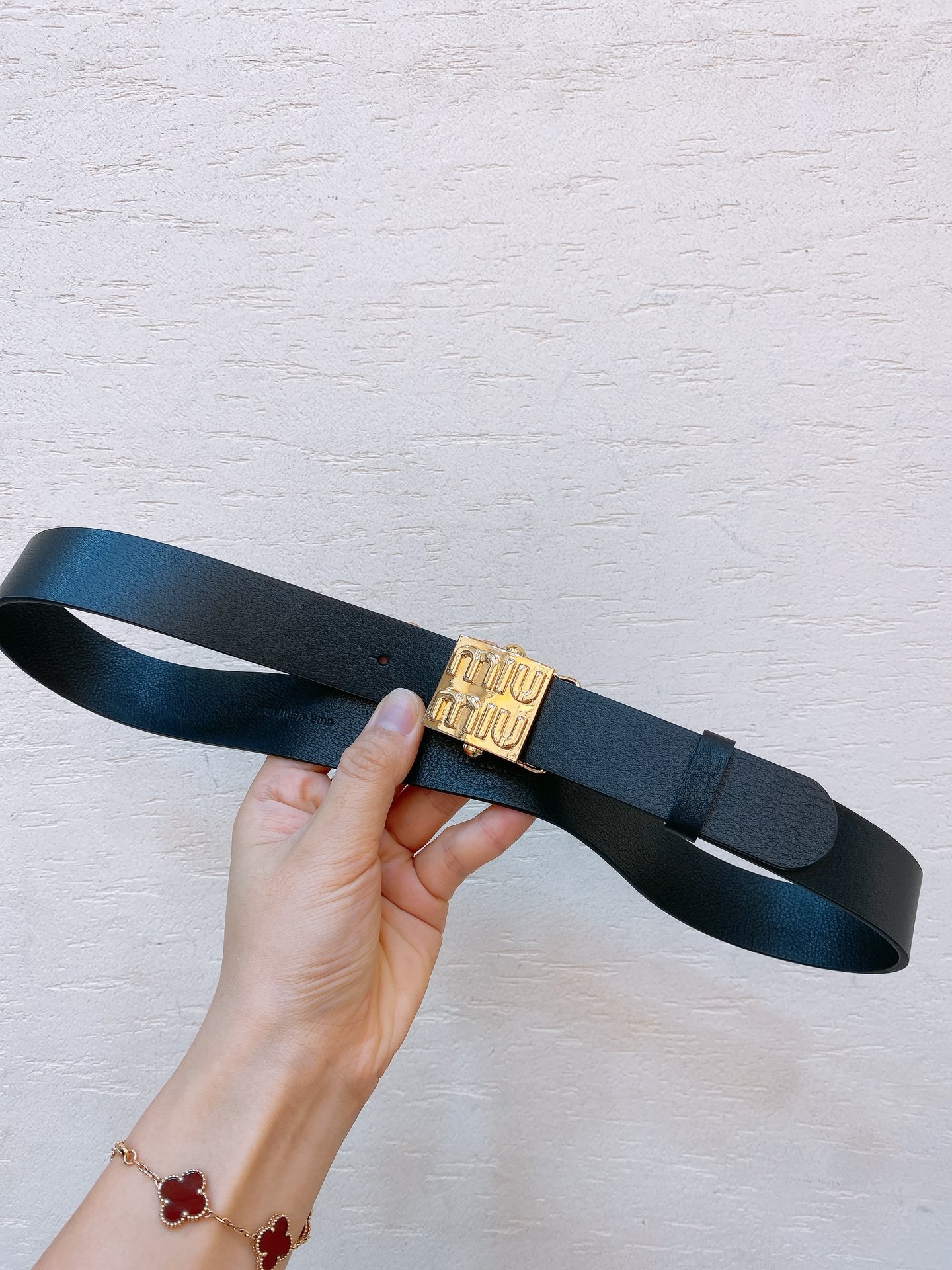Black leather belt with gold metal buckle engraved with Miu Miu