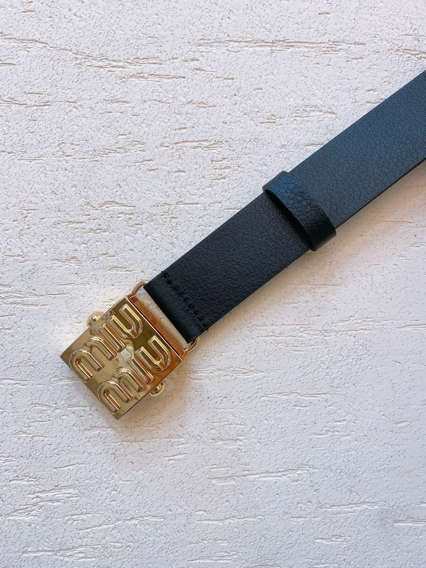 Black leather belt with gold metal buckle engraved with Miu Miu