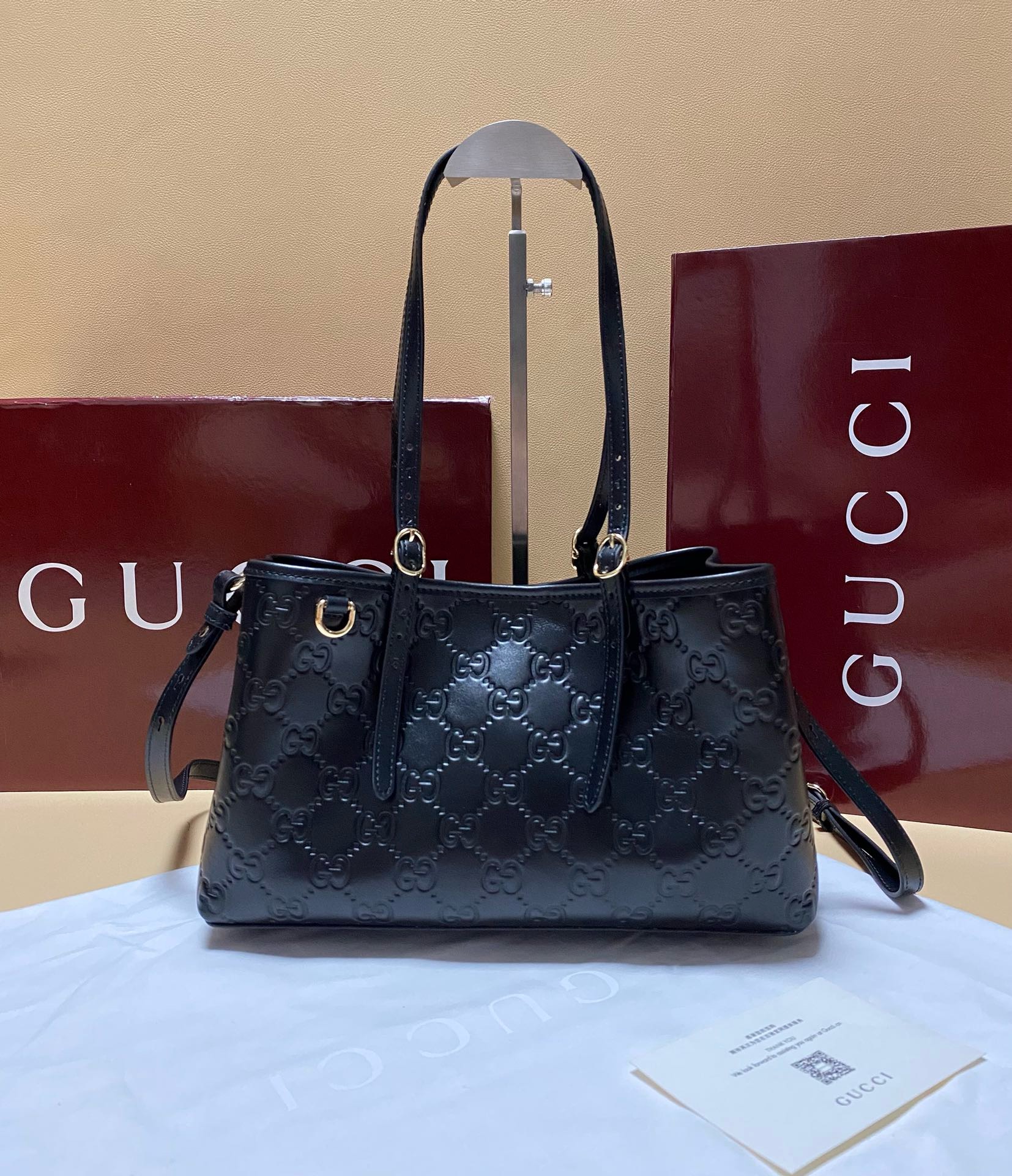 Gucci Black Embossed Tote bag, premium leather with GG monogram and gold hardware on a display stand.