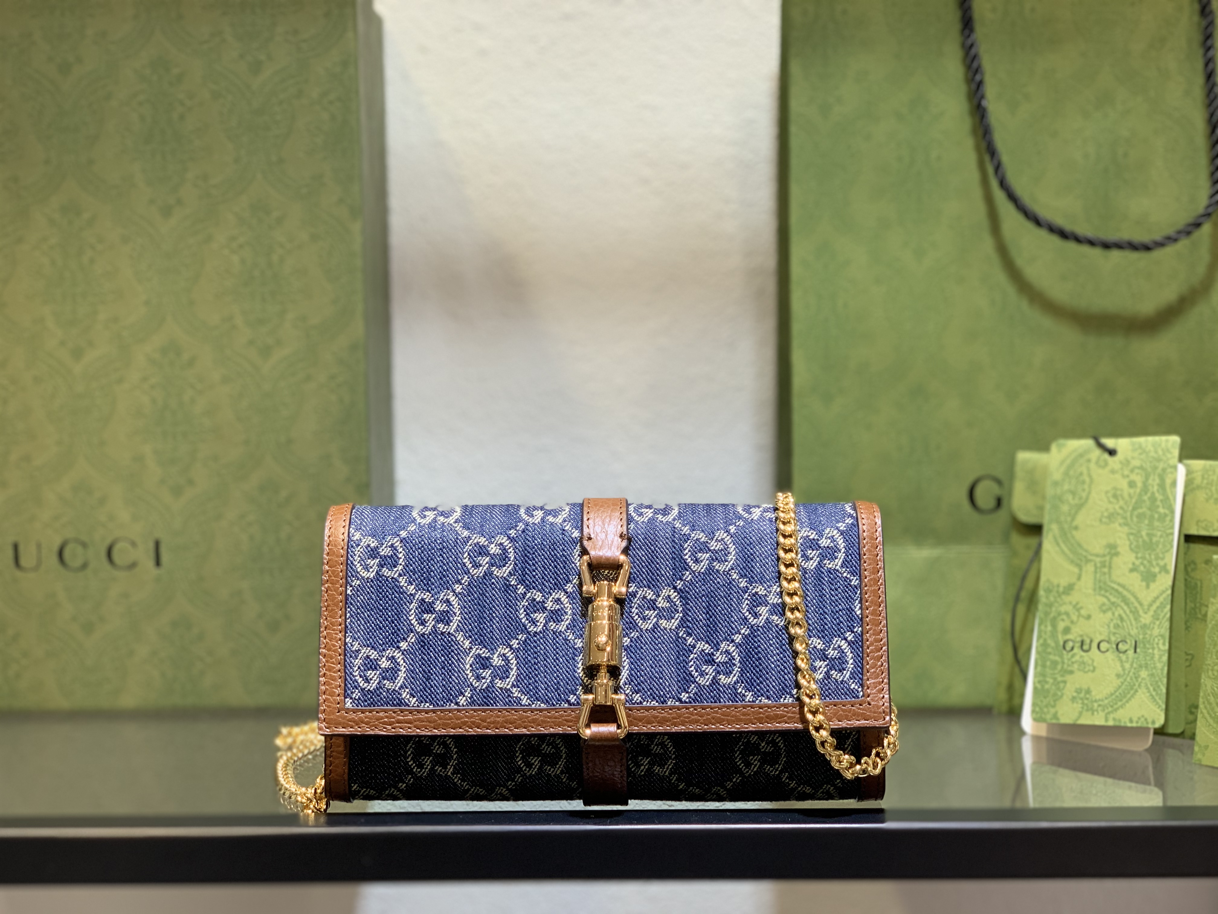 Gucci Jackie 1961 Blue Denim Chain Wallet with gold-tone hardware and brown leather trim on display.
