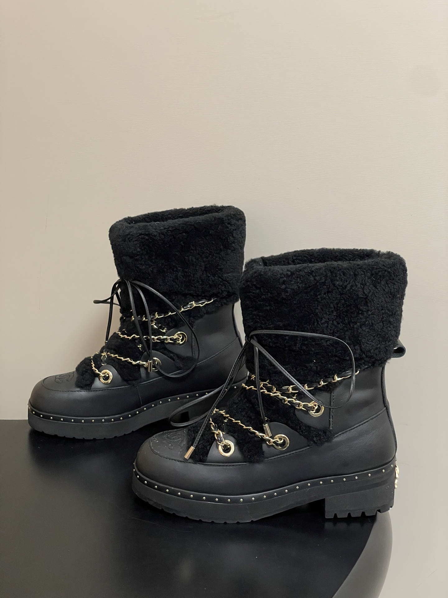 A pair of high-end black leather combat boots featuring thick black shearling trim and decorative gold chain laces. - Hình 4
