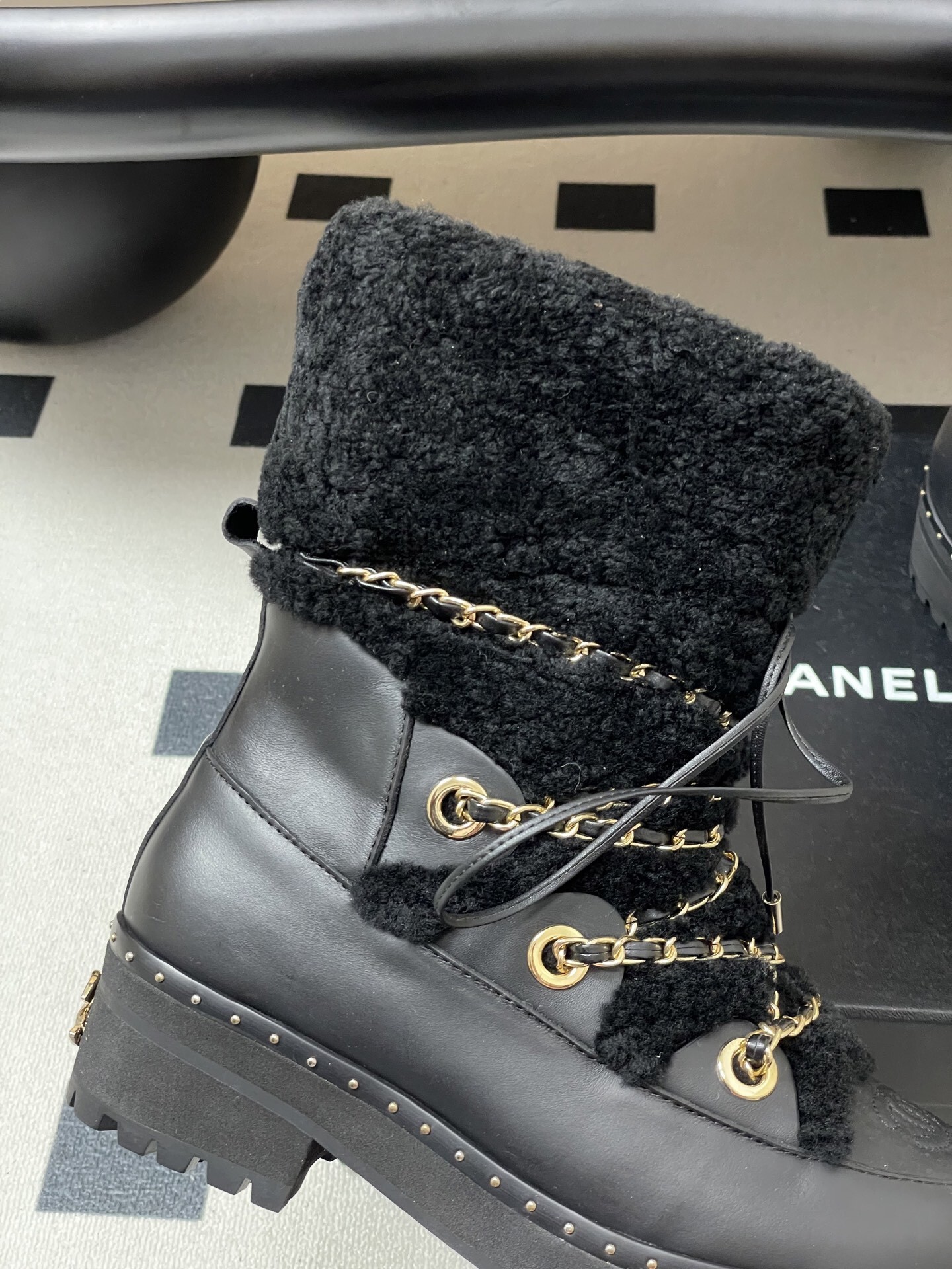 A pair of high-end black leather combat boots featuring thick black shearling trim and decorative gold chain laces. - Hình 2