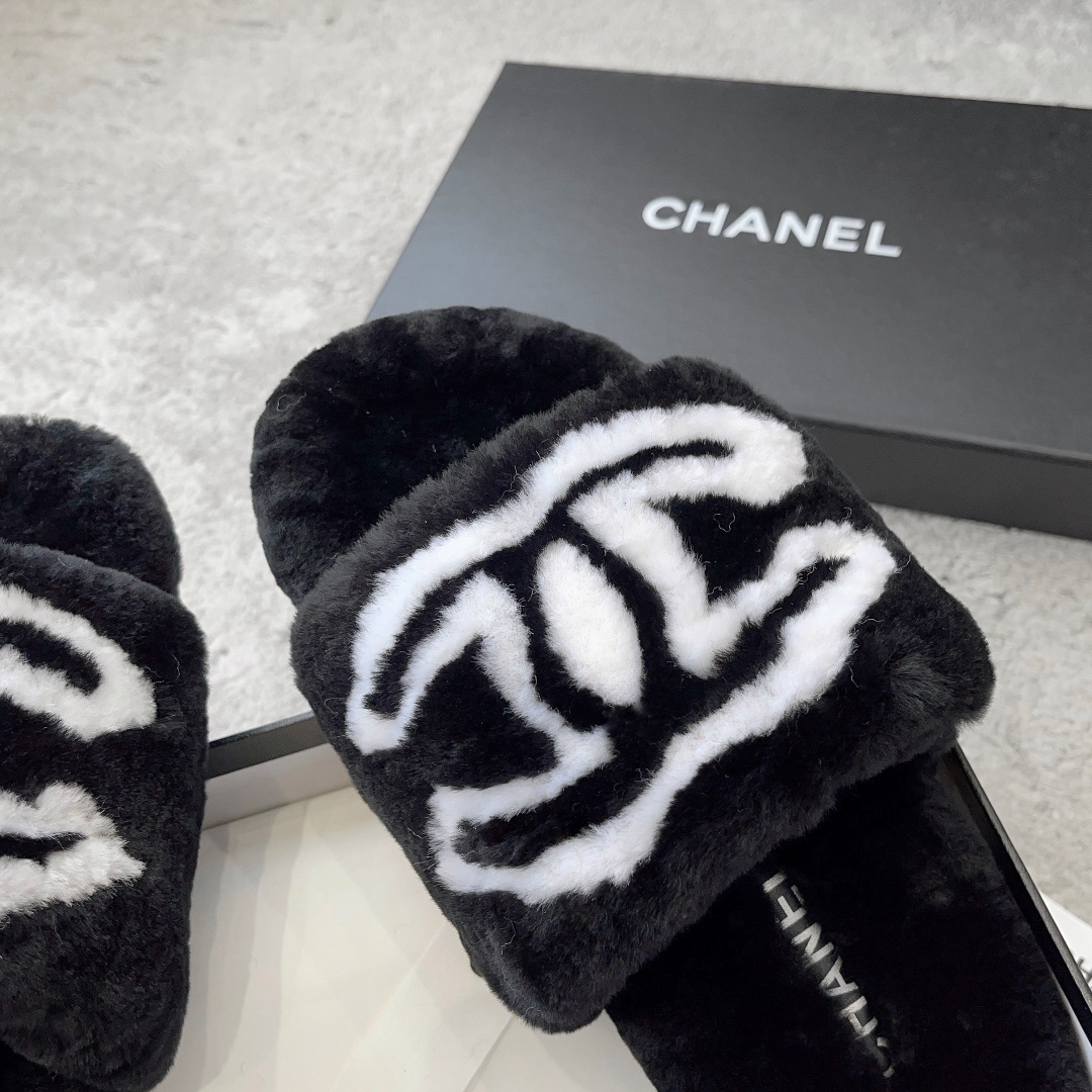 A pair of black Chanel plush fur slides featuring a large white CC logo, presented on a black Chanel shoebox with white ribbon. - Hình 6