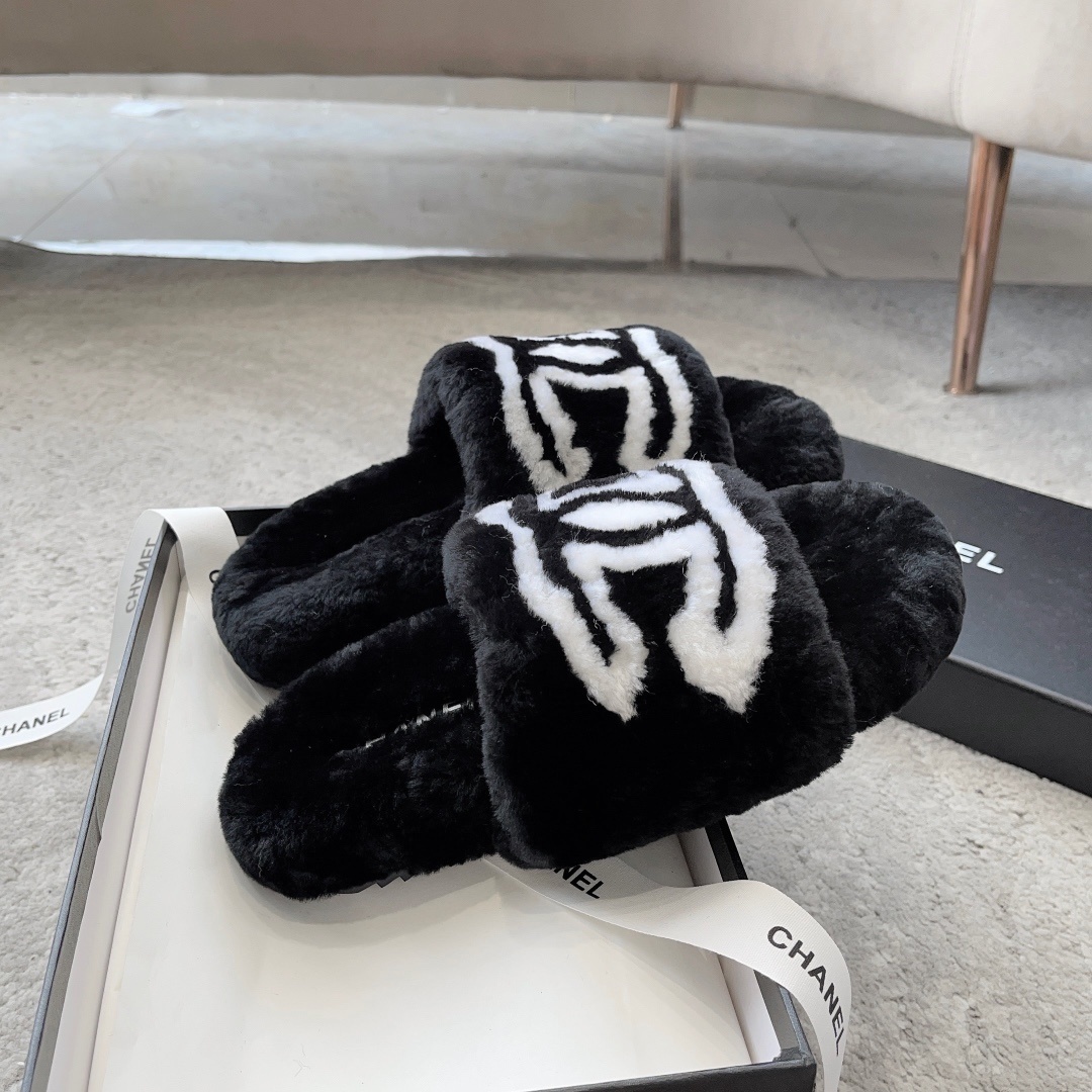 A pair of black Chanel plush fur slides featuring a large white CC logo, presented on a black Chanel shoebox with white ribbon. - Hình 5