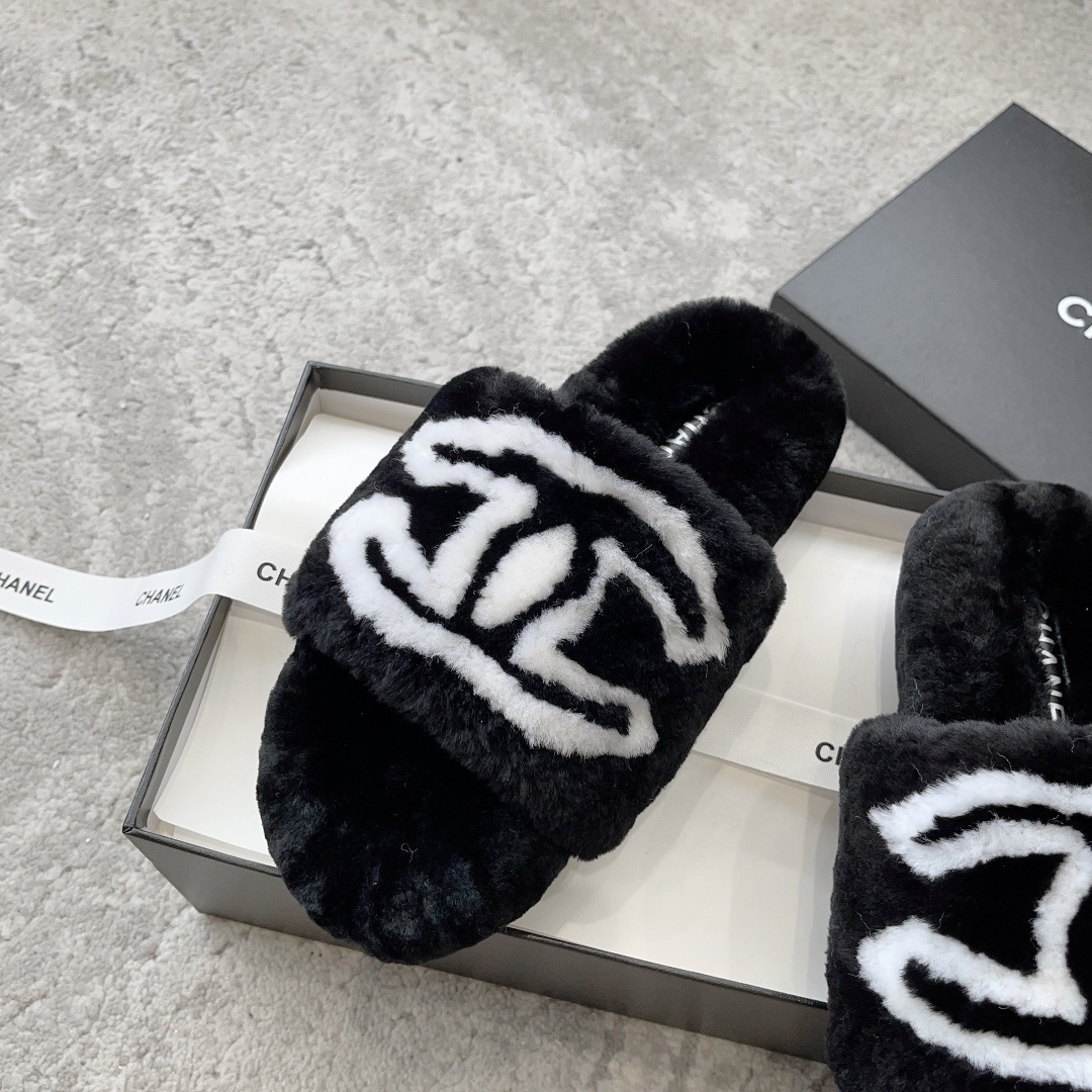 A pair of black Chanel plush fur slides featuring a large white CC logo, presented on a black Chanel shoebox with white ribbon. - Hình 4