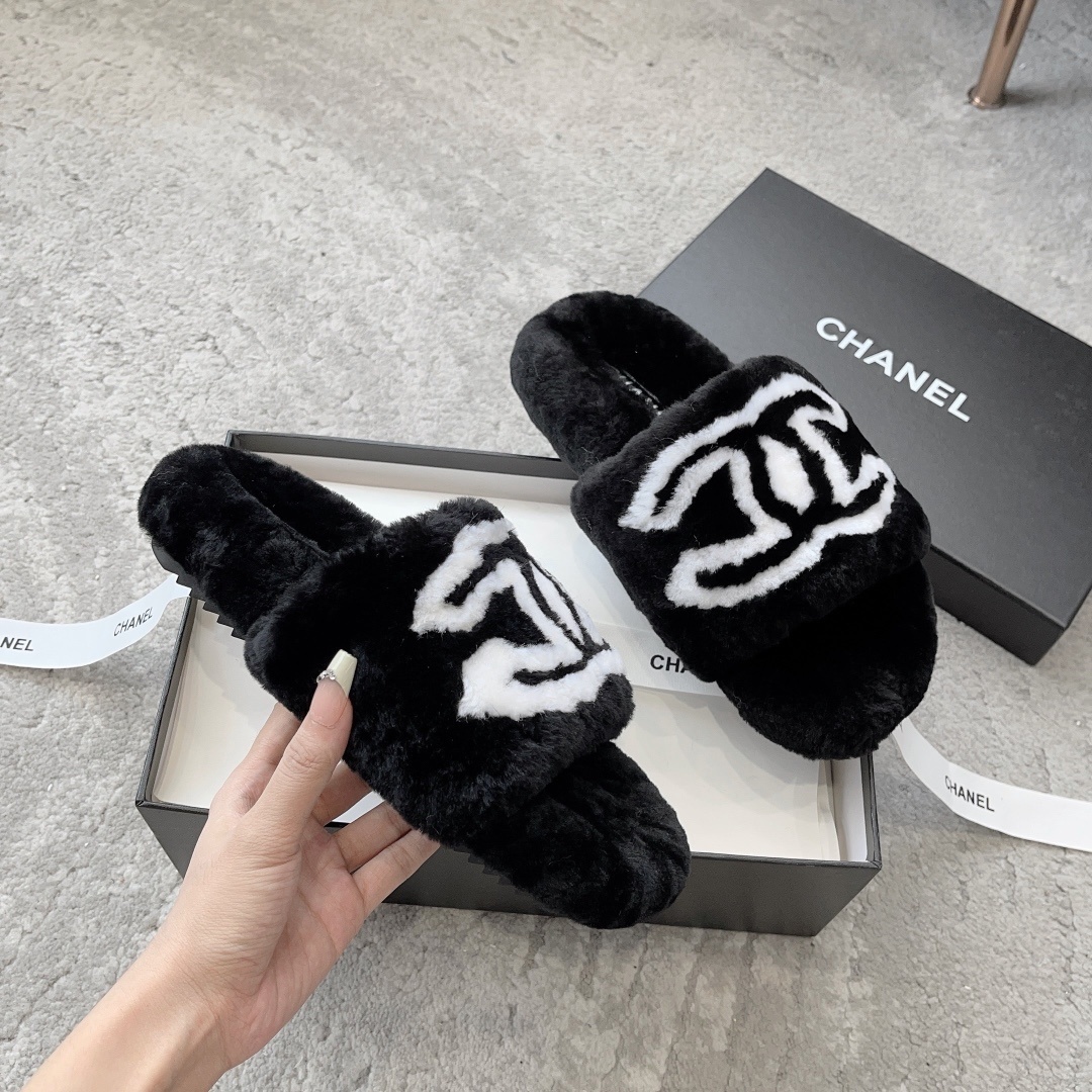 A pair of black Chanel plush fur slides featuring a large white CC logo, presented on a black Chanel shoebox with white ribbon. - Hình 3