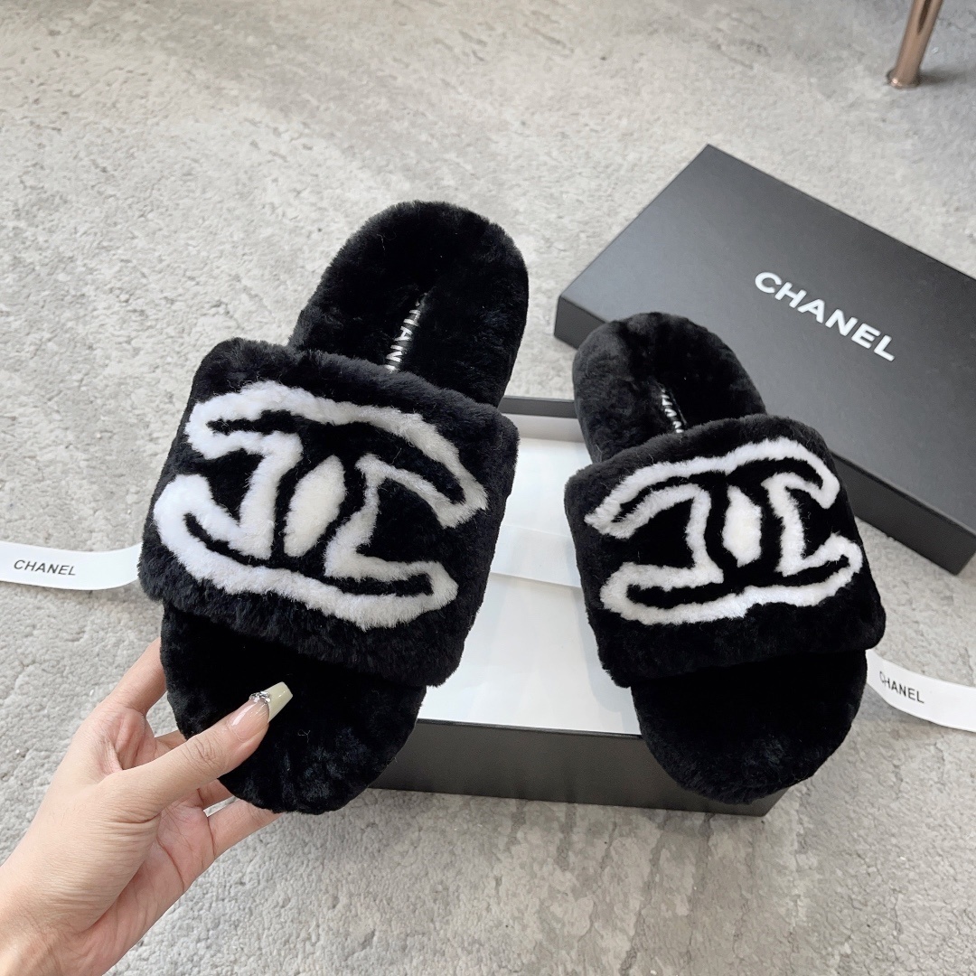 A pair of black Chanel plush fur slides featuring a large white CC logo, presented on a black Chanel shoebox with white ribbon. - Hình 2