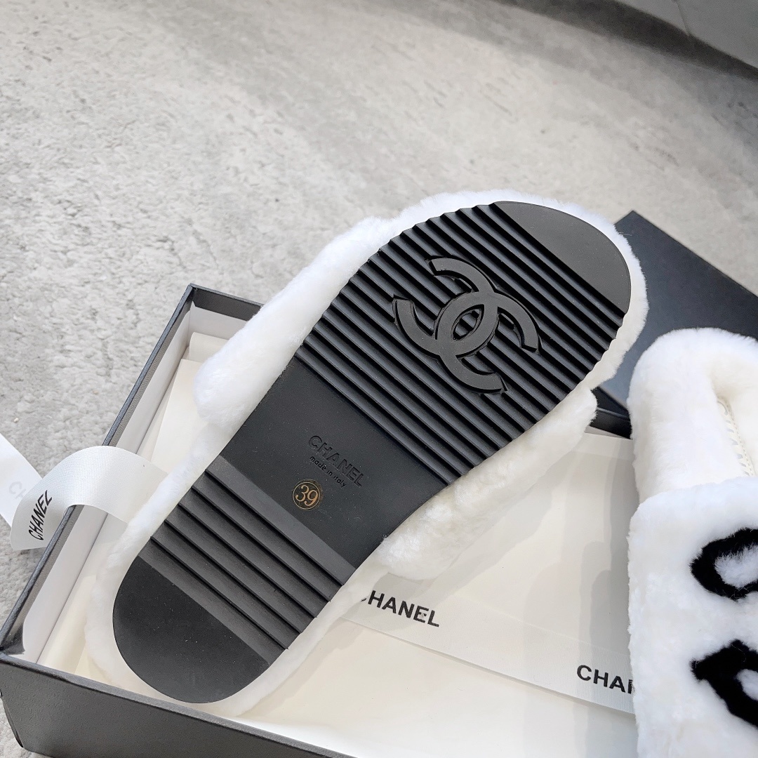 A pair of white plush faux fur slippers with a black interlocking CC logo resting on a luxury black gift box - Hình 9