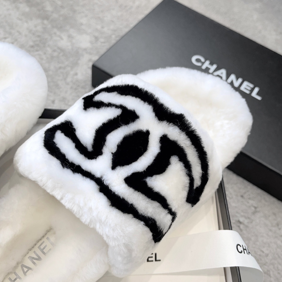 A pair of white plush faux fur slippers with a black interlocking CC logo resting on a luxury black gift box - Hình 6