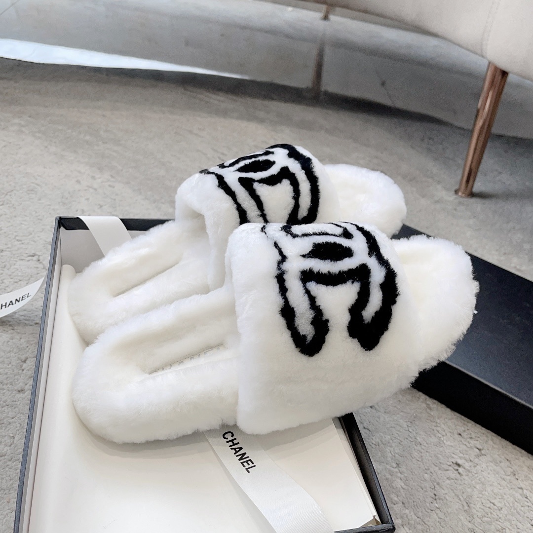 A pair of white plush faux fur slippers with a black interlocking CC logo resting on a luxury black gift box - Hình 4