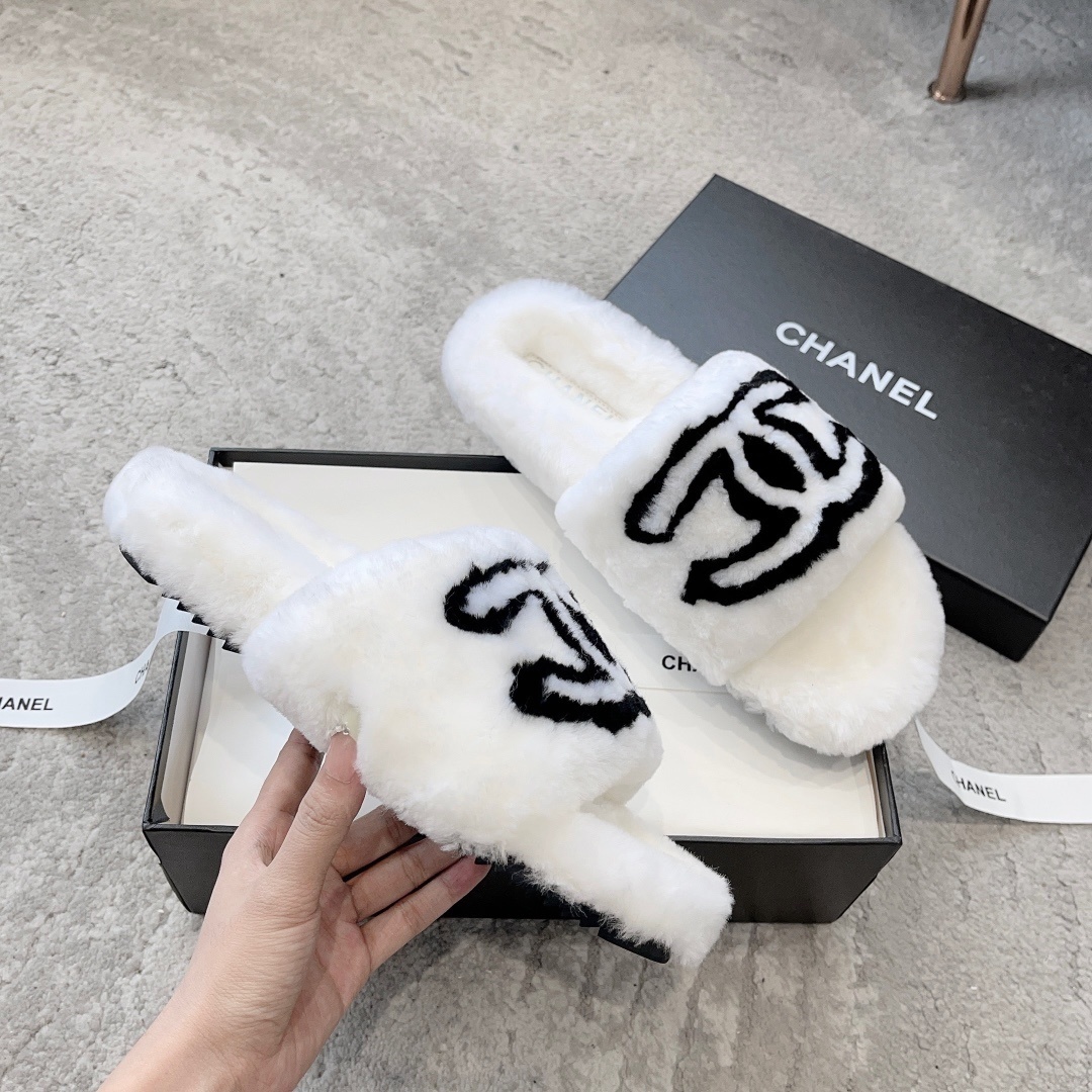 A pair of white plush faux fur slippers with a black interlocking CC logo resting on a luxury black gift box - Hình 3