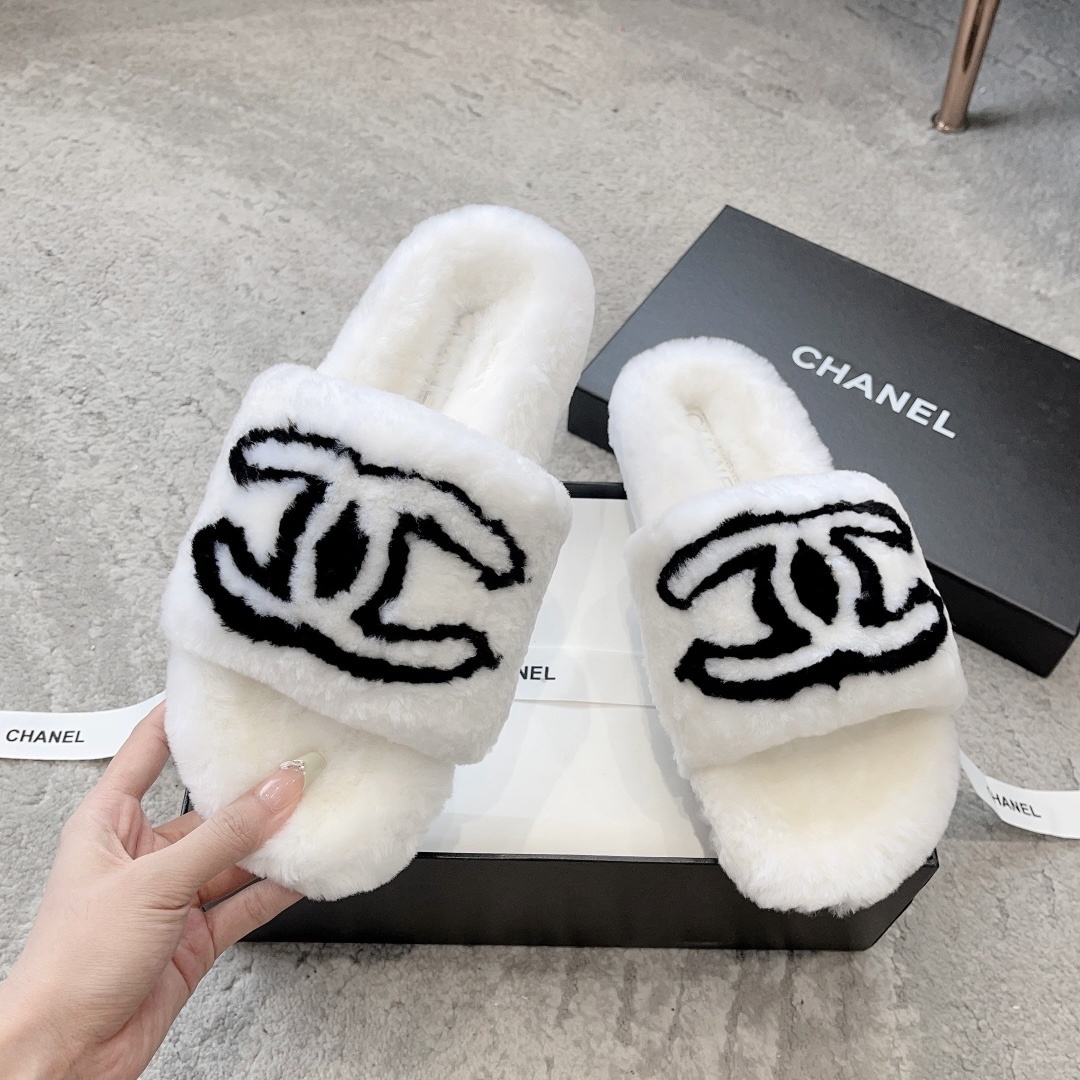 A pair of white plush faux fur slippers with a black interlocking CC logo resting on a luxury black gift box - Hình 2