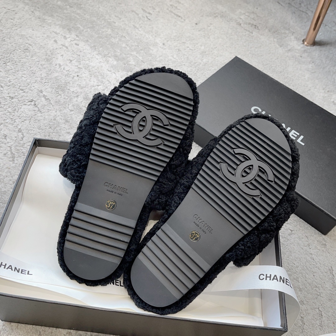 A pair of black fluffy shearling-style slippers with a white interlocking CC logo sitting on a black designer box - Hình 9