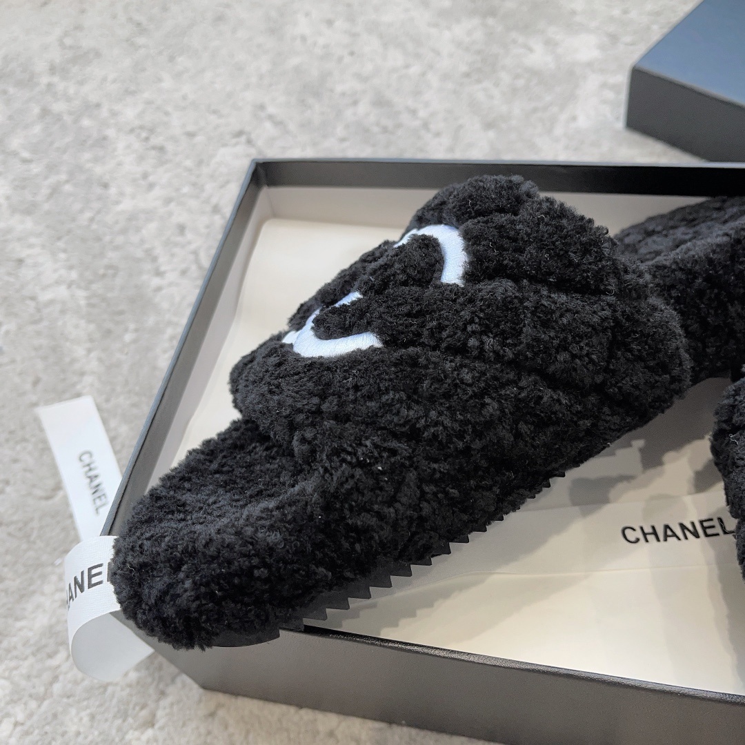 A pair of black fluffy shearling-style slippers with a white interlocking CC logo sitting on a black designer box - Hình 7