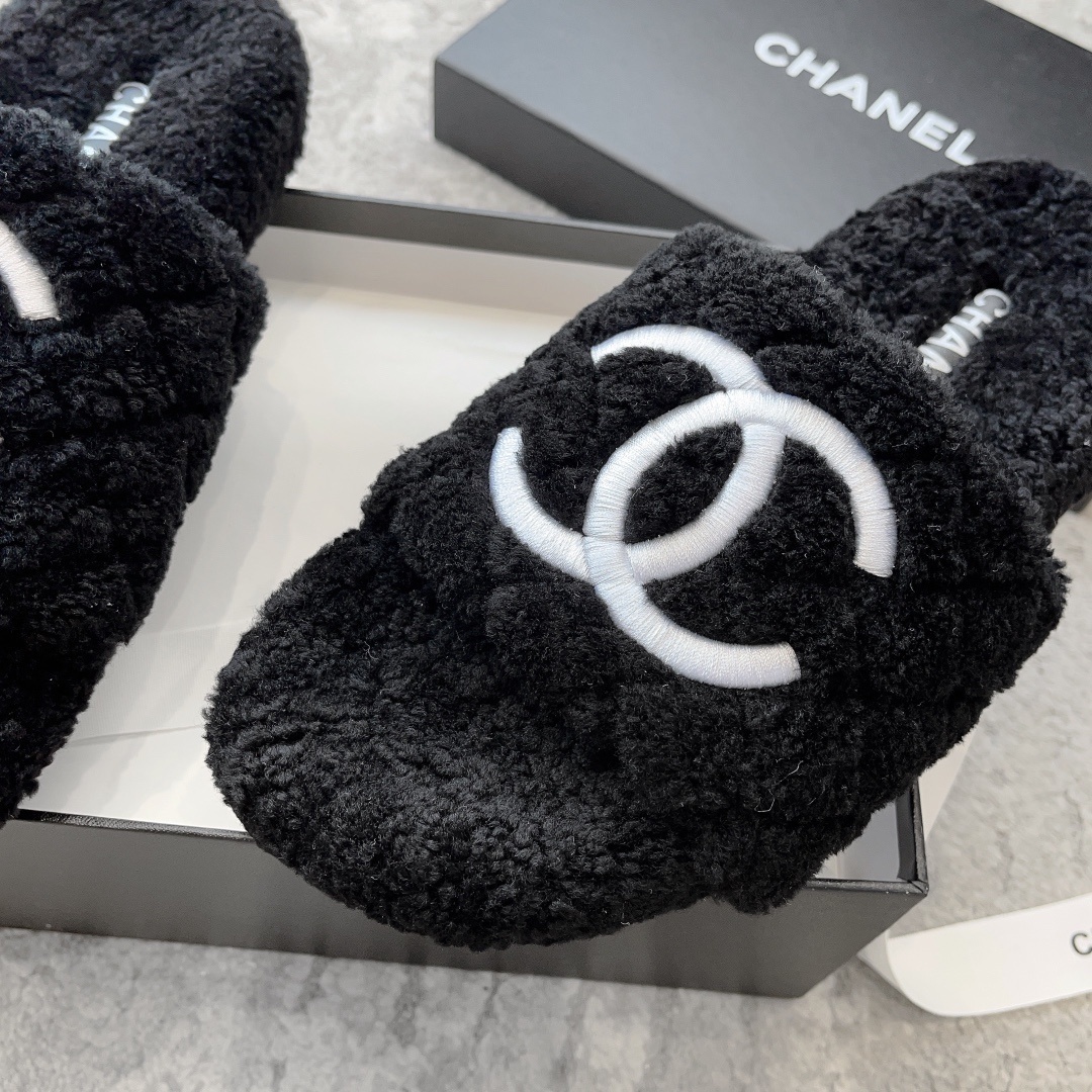 A pair of black fluffy shearling-style slippers with a white interlocking CC logo sitting on a black designer box - Hình 6