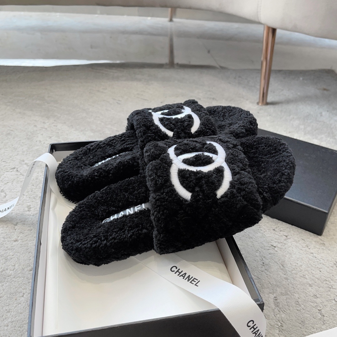 A pair of black fluffy shearling-style slippers with a white interlocking CC logo sitting on a black designer box - Hình 5