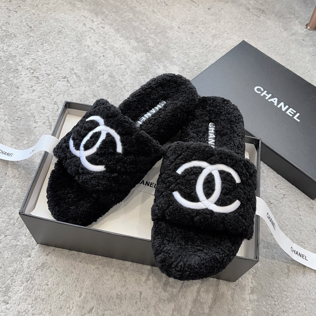 A pair of black fluffy shearling-style slippers with a white interlocking CC logo sitting on a black designer box - Hình 4