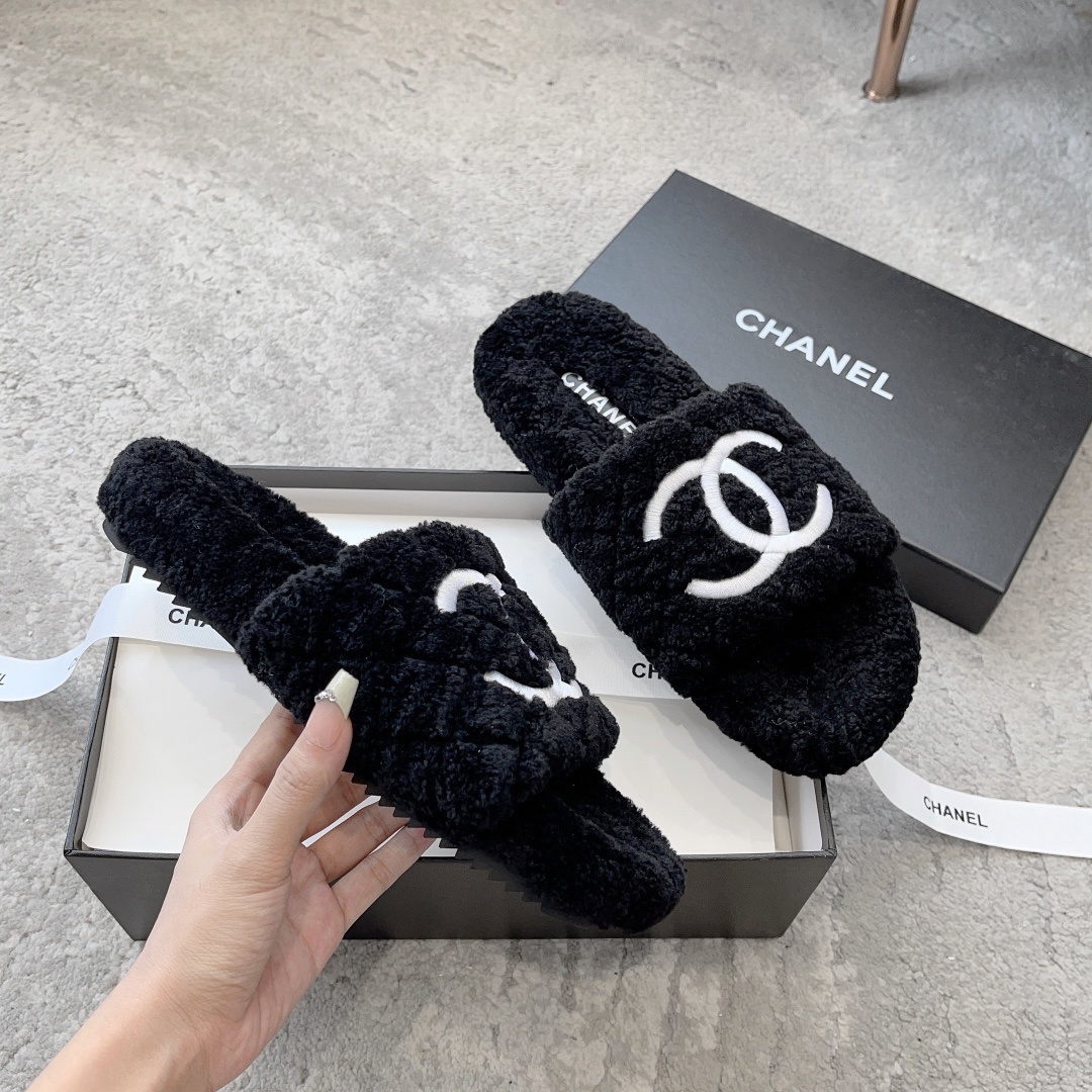 A pair of black fluffy shearling-style slippers with a white interlocking CC logo sitting on a black designer box - Hình 3