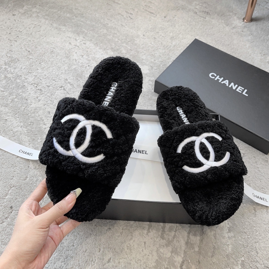A pair of black fluffy shearling-style slippers with a white interlocking CC logo sitting on a black designer box - Hình 2