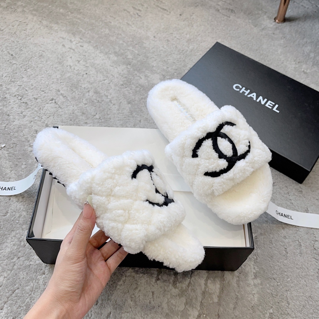 A pair of premium white fuzzy shearling slides with a black interlaced logo displayed on a designer shoebox. - Hình 3