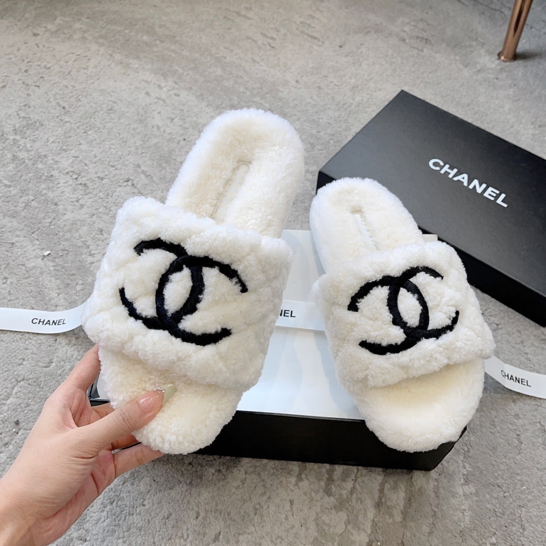 A pair of premium white fuzzy shearling slides with a black interlaced logo displayed on a designer shoebox. - Hình 2