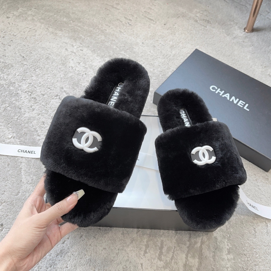 A pair of black fluffy faux fur slides with a white interlocking CC logo placed on a black designer shoe box. - Hình 2