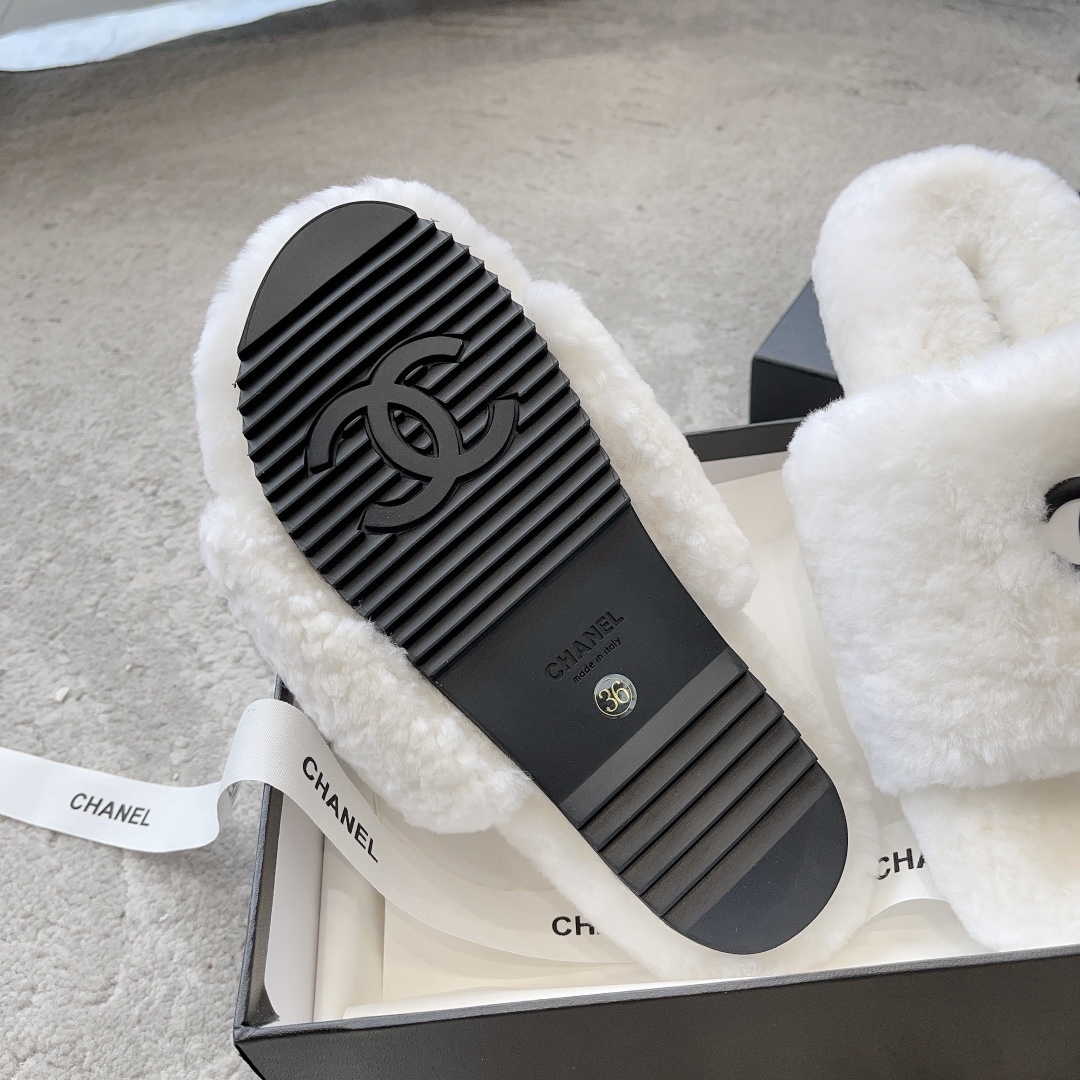 A pair of fluffy white faux fur slippers featuring a black interlaced logo, presented on a black designer box. - Hình 9