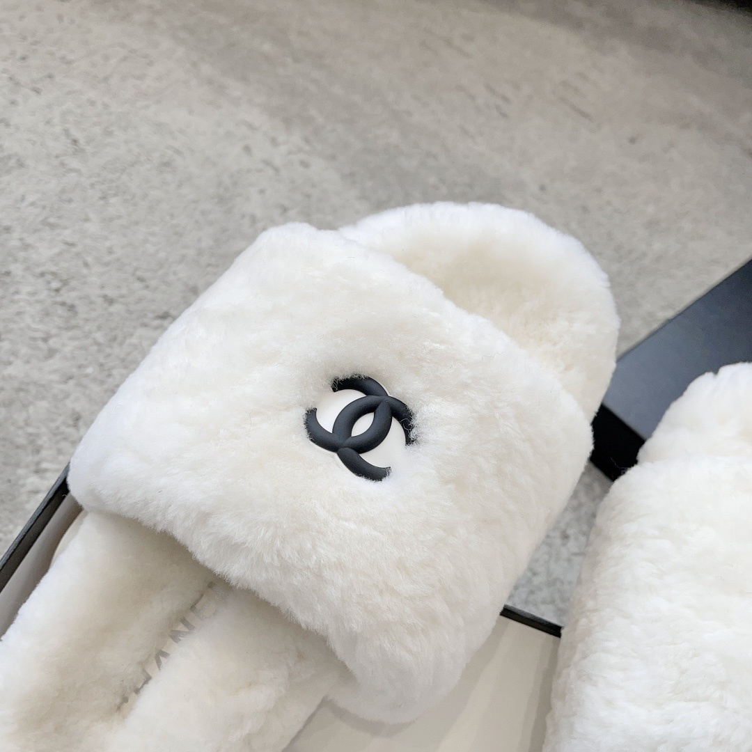 A pair of fluffy white faux fur slippers featuring a black interlaced logo, presented on a black designer box. - Hình 6