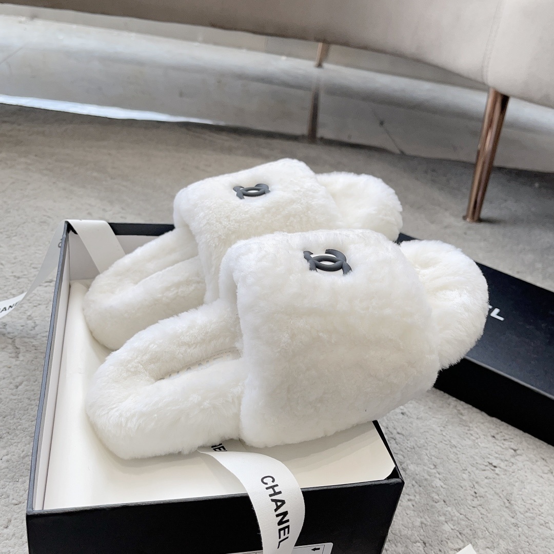 A pair of fluffy white faux fur slippers featuring a black interlaced logo, presented on a black designer box. - Hình 5
