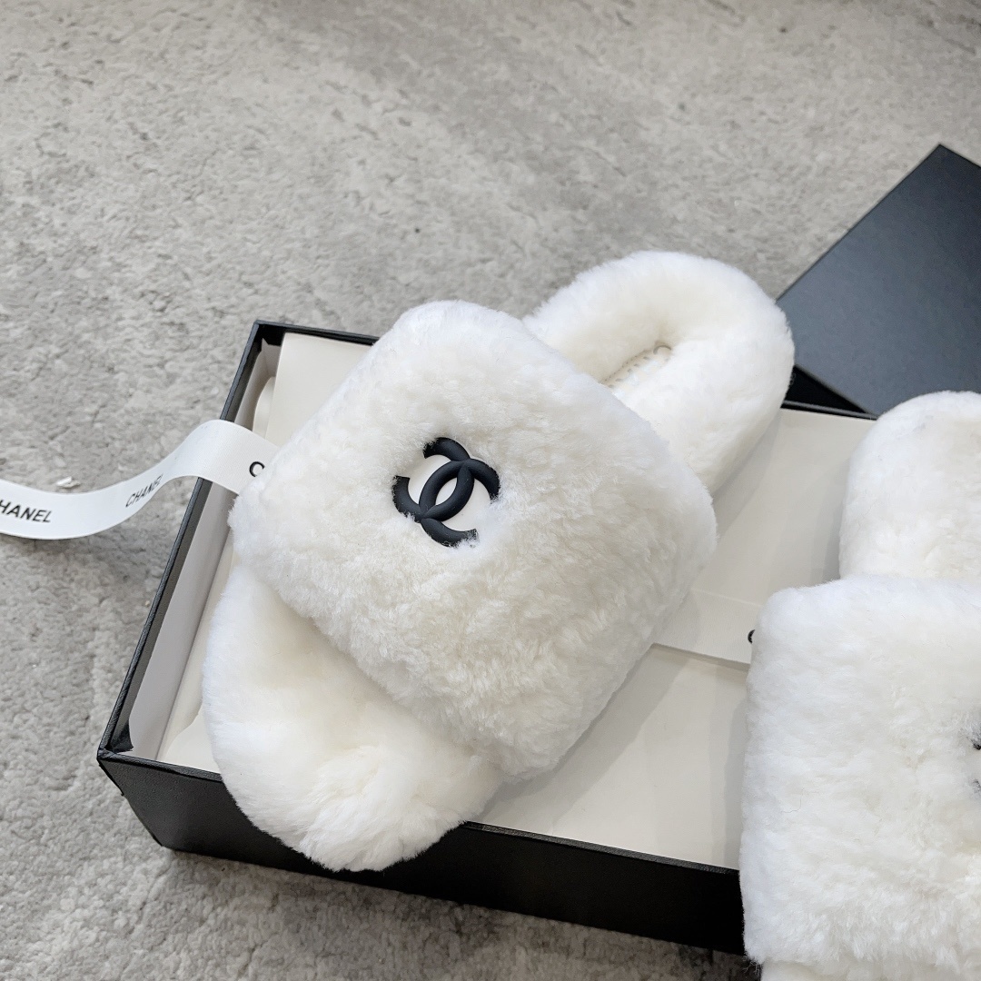 A pair of fluffy white faux fur slippers featuring a black interlaced logo, presented on a black designer box. - Hình 4