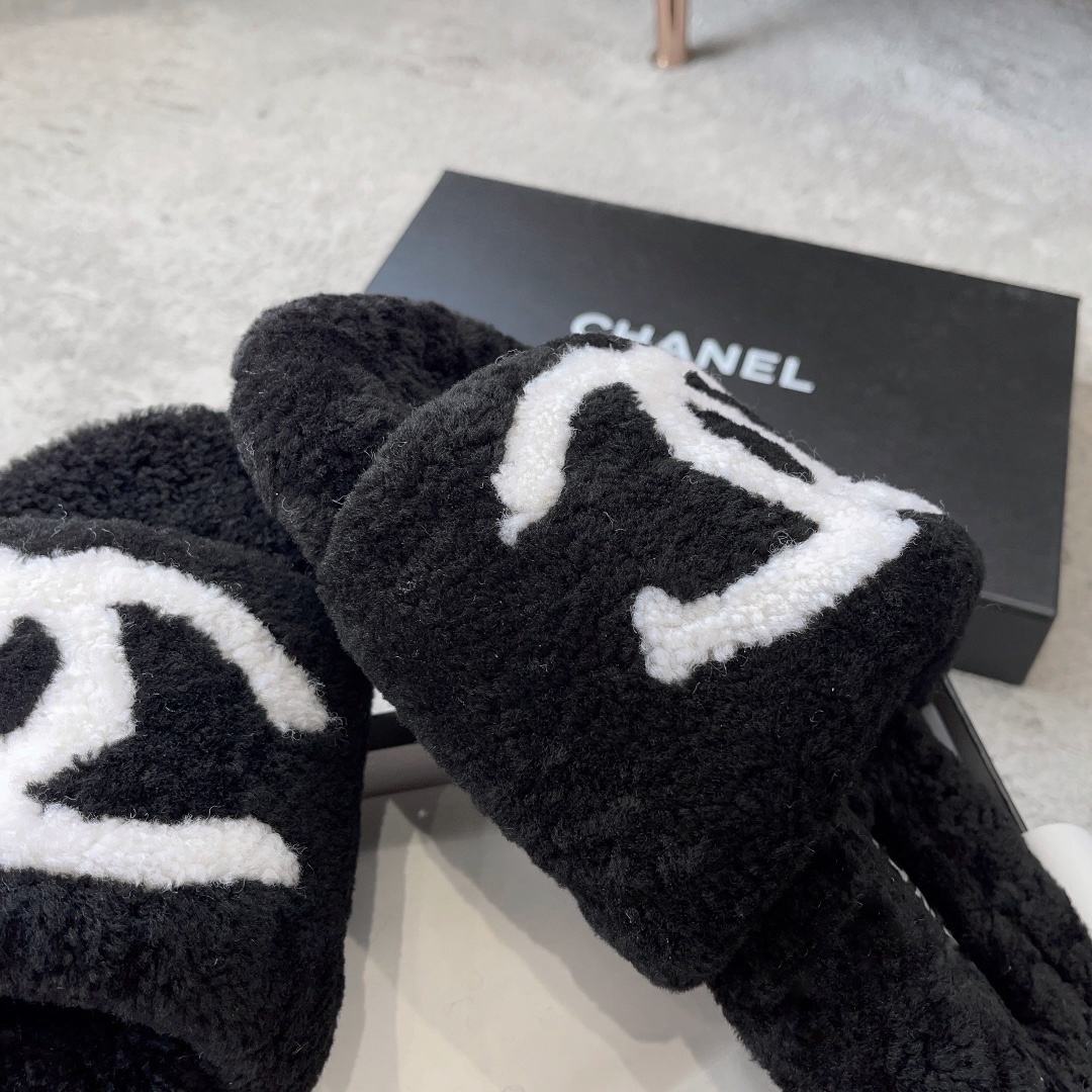 A pair of black fuzzy Chanel shearling slippers with a large white interlocking CC logo, presented in a black Chanel box with a white ribbon. - Hình 6