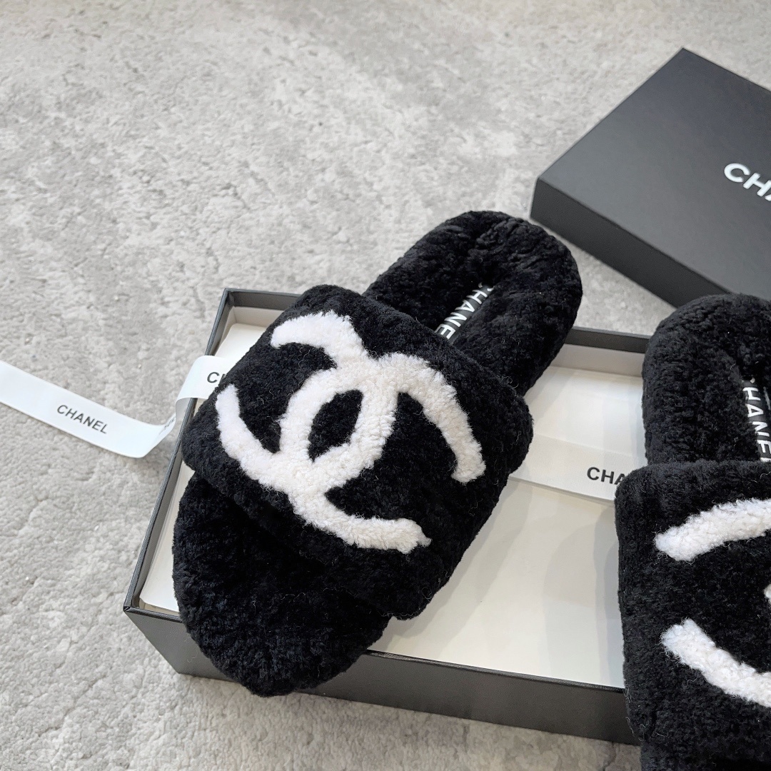 A pair of black fuzzy Chanel shearling slippers with a large white interlocking CC logo, presented in a black Chanel box with a white ribbon. - Hình 4
