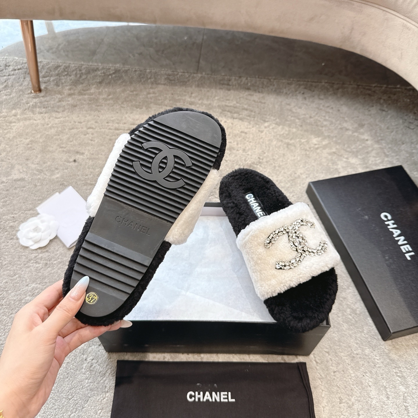 A pair of black and white Chanel shearling slides with crystal-encrusted CC logos presented in a black designer box. - Hình 9