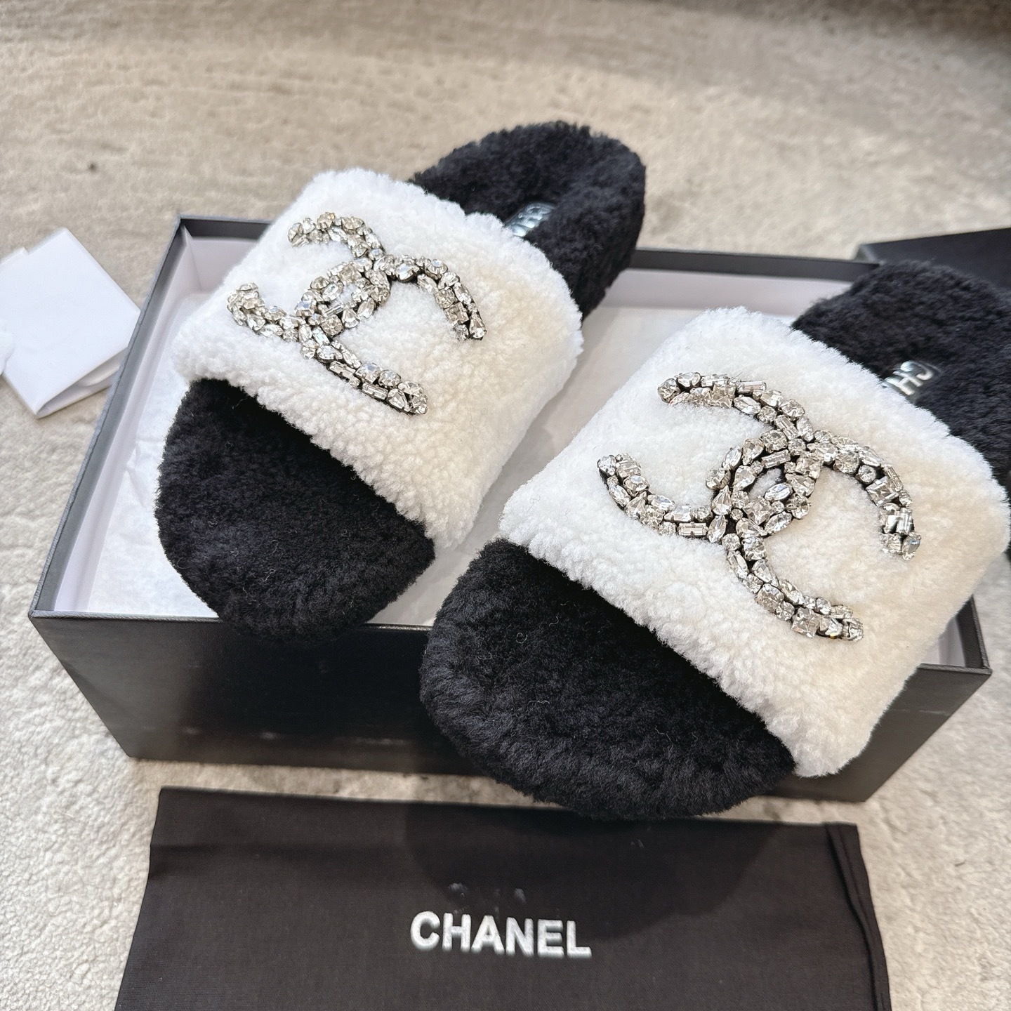 A pair of black and white Chanel shearling slides with crystal-encrusted CC logos presented in a black designer box. - Hình 7