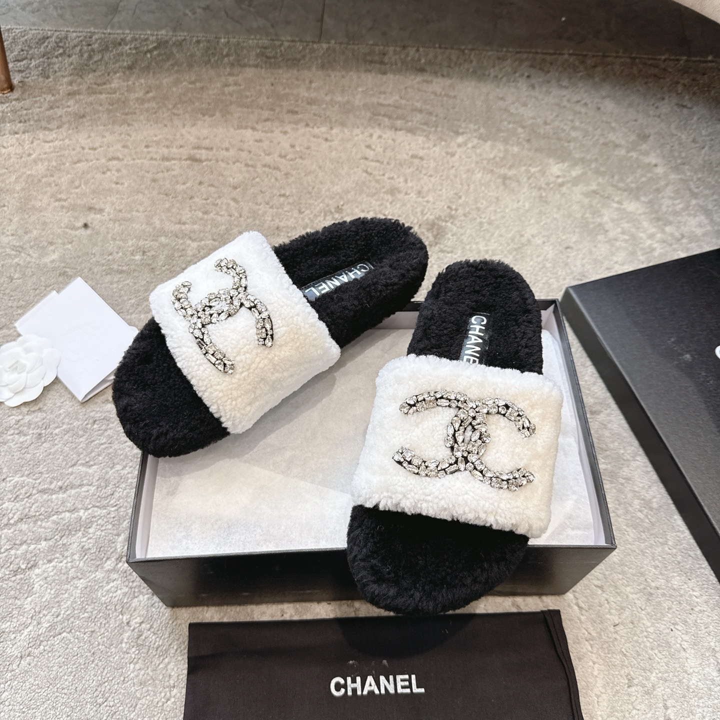 A pair of black and white Chanel shearling slides with crystal-encrusted CC logos presented in a black designer box. - Hình 5