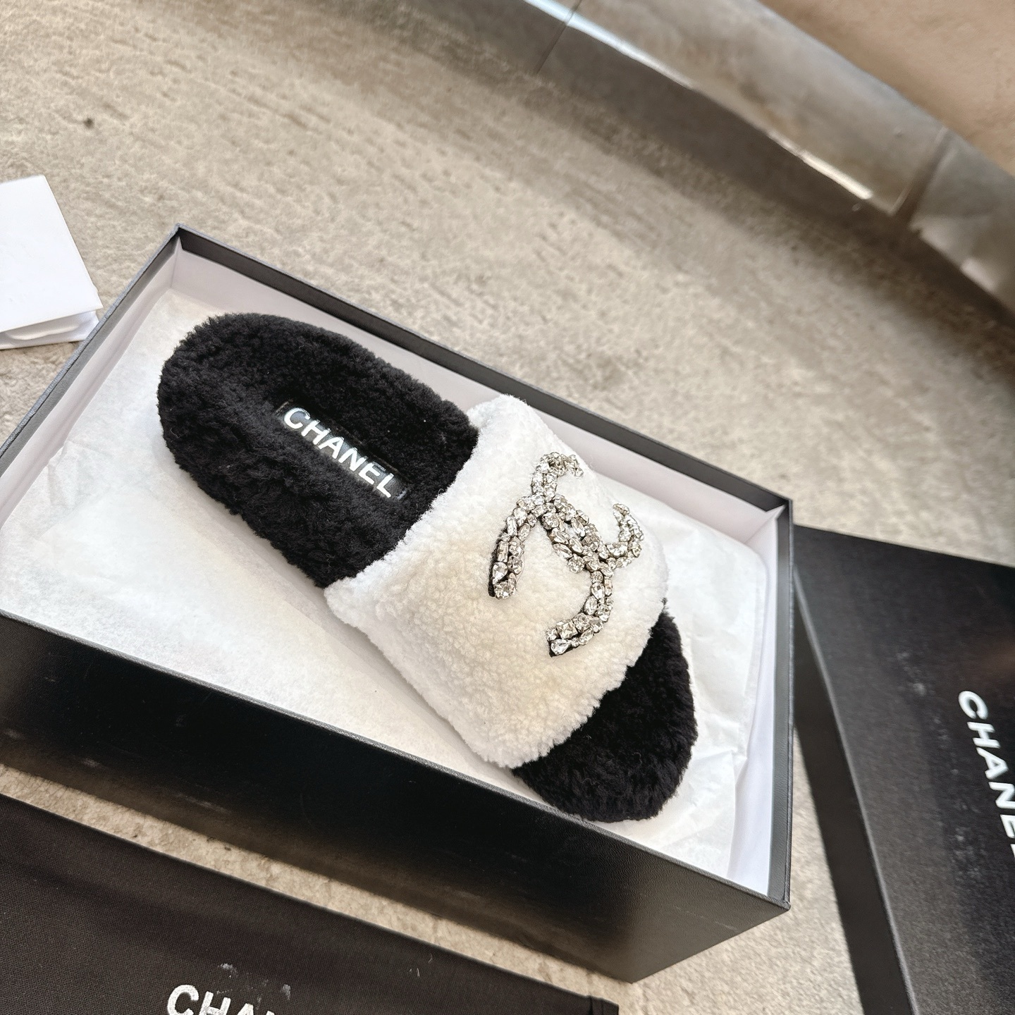 A pair of black and white Chanel shearling slides with crystal-encrusted CC logos presented in a black designer box. - Hình 4
