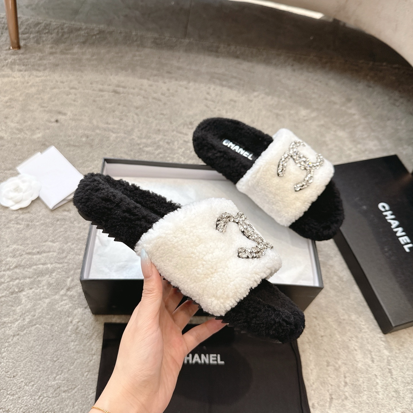 A pair of black and white Chanel shearling slides with crystal-encrusted CC logos presented in a black designer box. - Hình 3