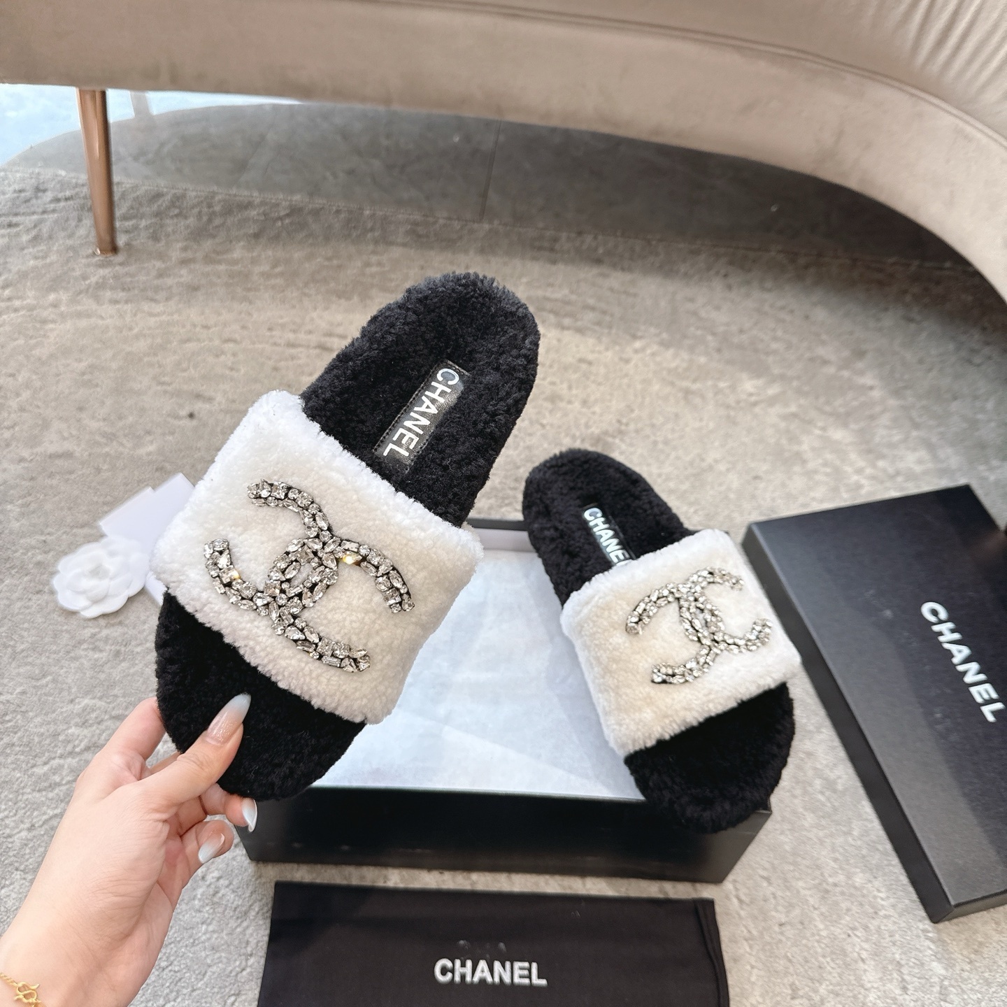 A pair of black and white Chanel shearling slides with crystal-encrusted CC logos presented in a black designer box. - Hình 2