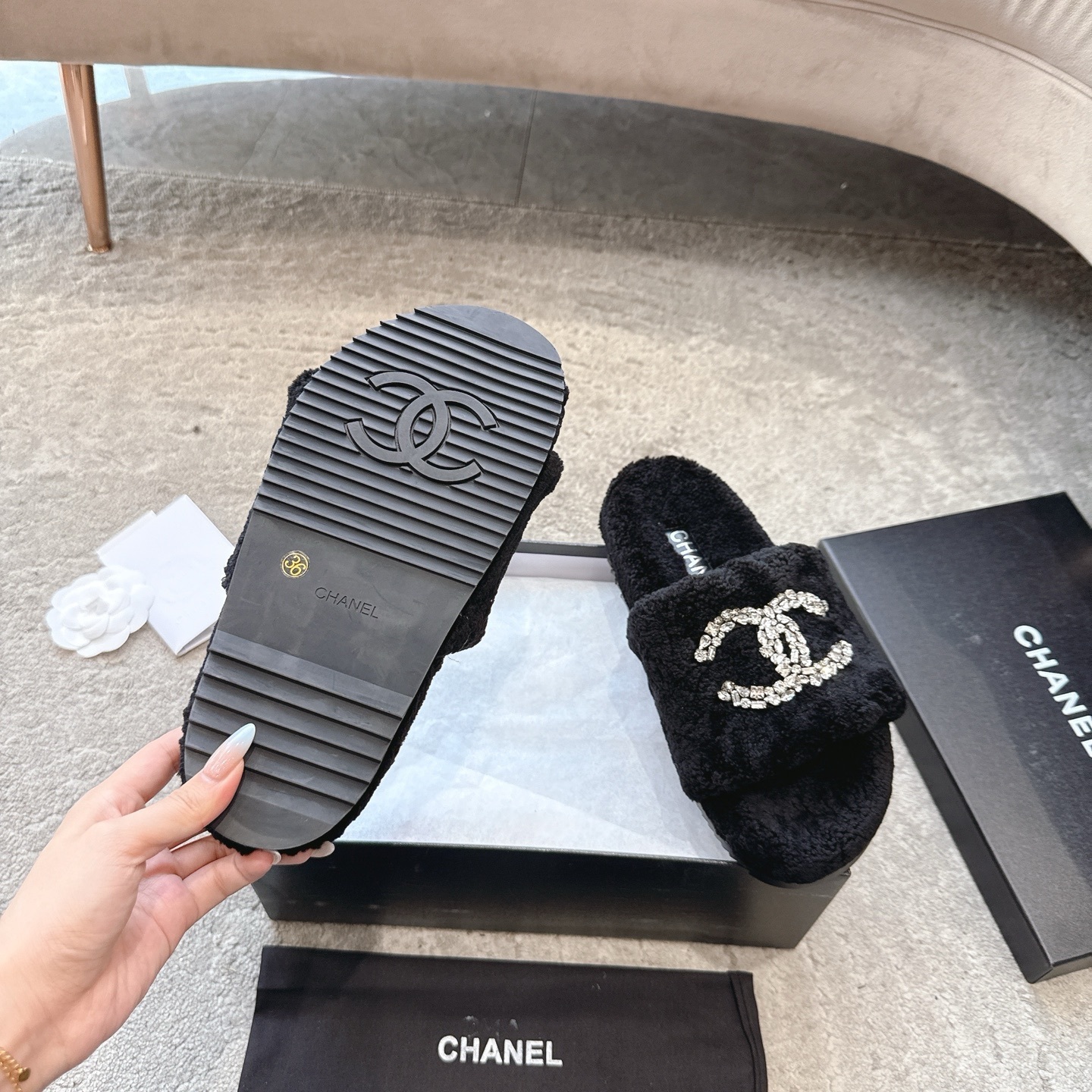 A pair of black fuzzy Chanel slides with large crystal interlocking CC logos on top, presented in a black brand box. - Hình 9