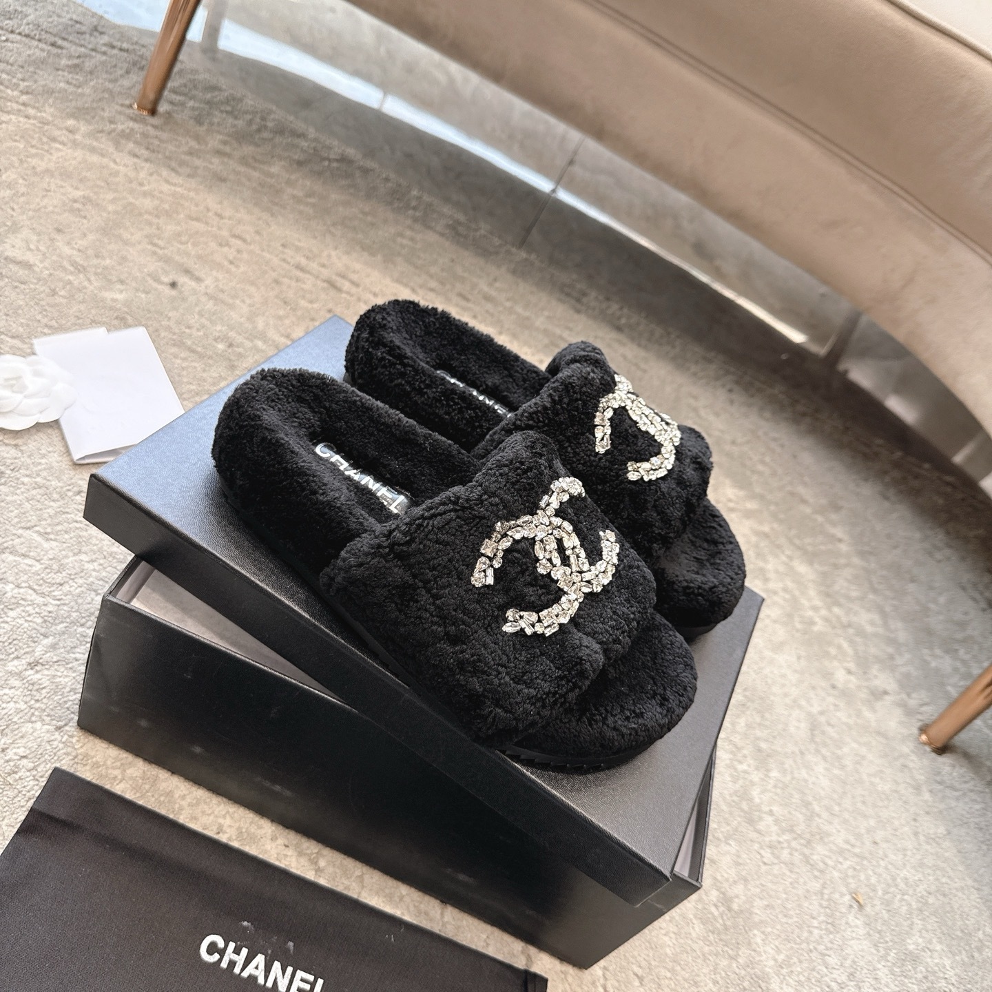 A pair of black fuzzy Chanel slides with large crystal interlocking CC logos on top, presented in a black brand box. - Hình 6