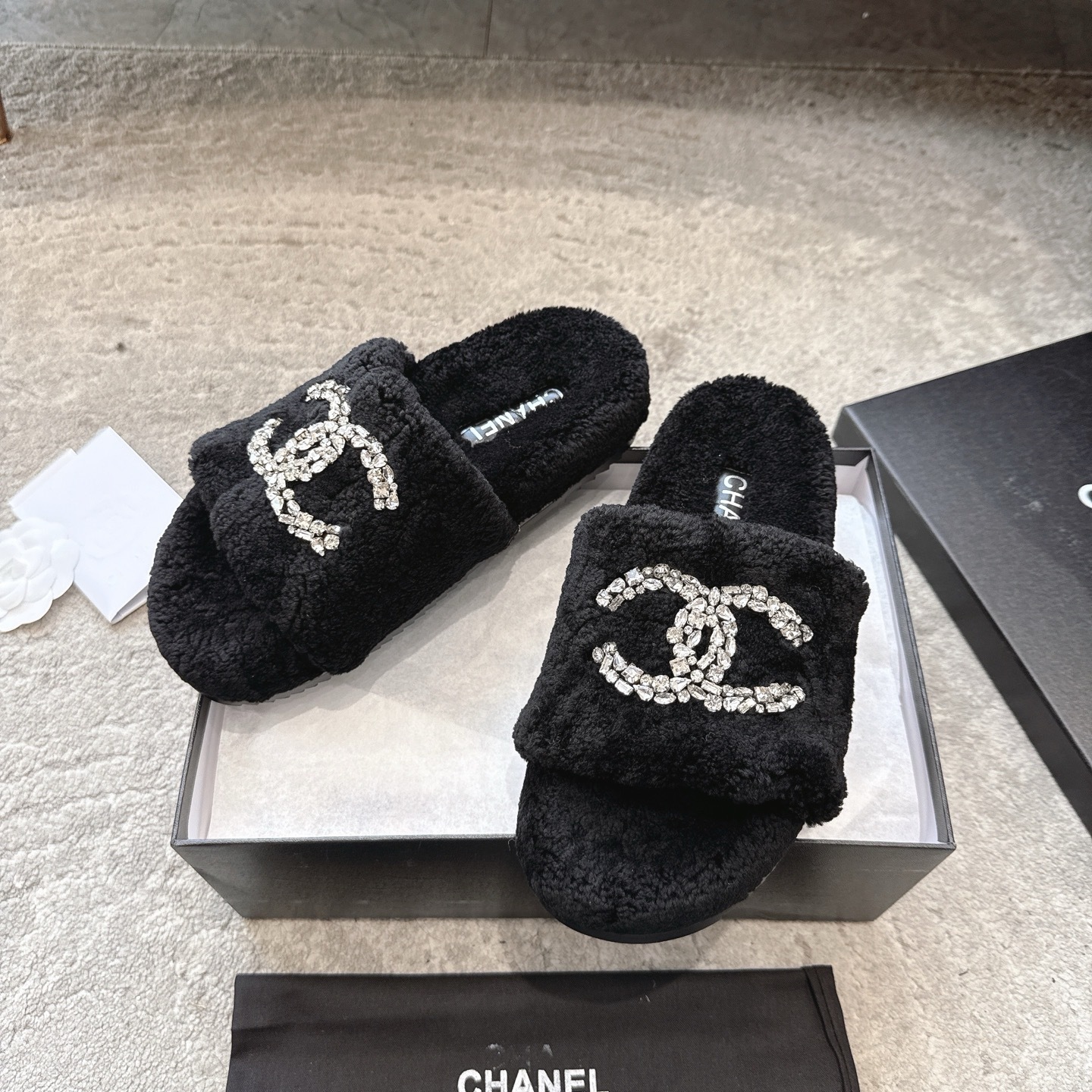 A pair of black fuzzy Chanel slides with large crystal interlocking CC logos on top, presented in a black brand box. - Hình 5
