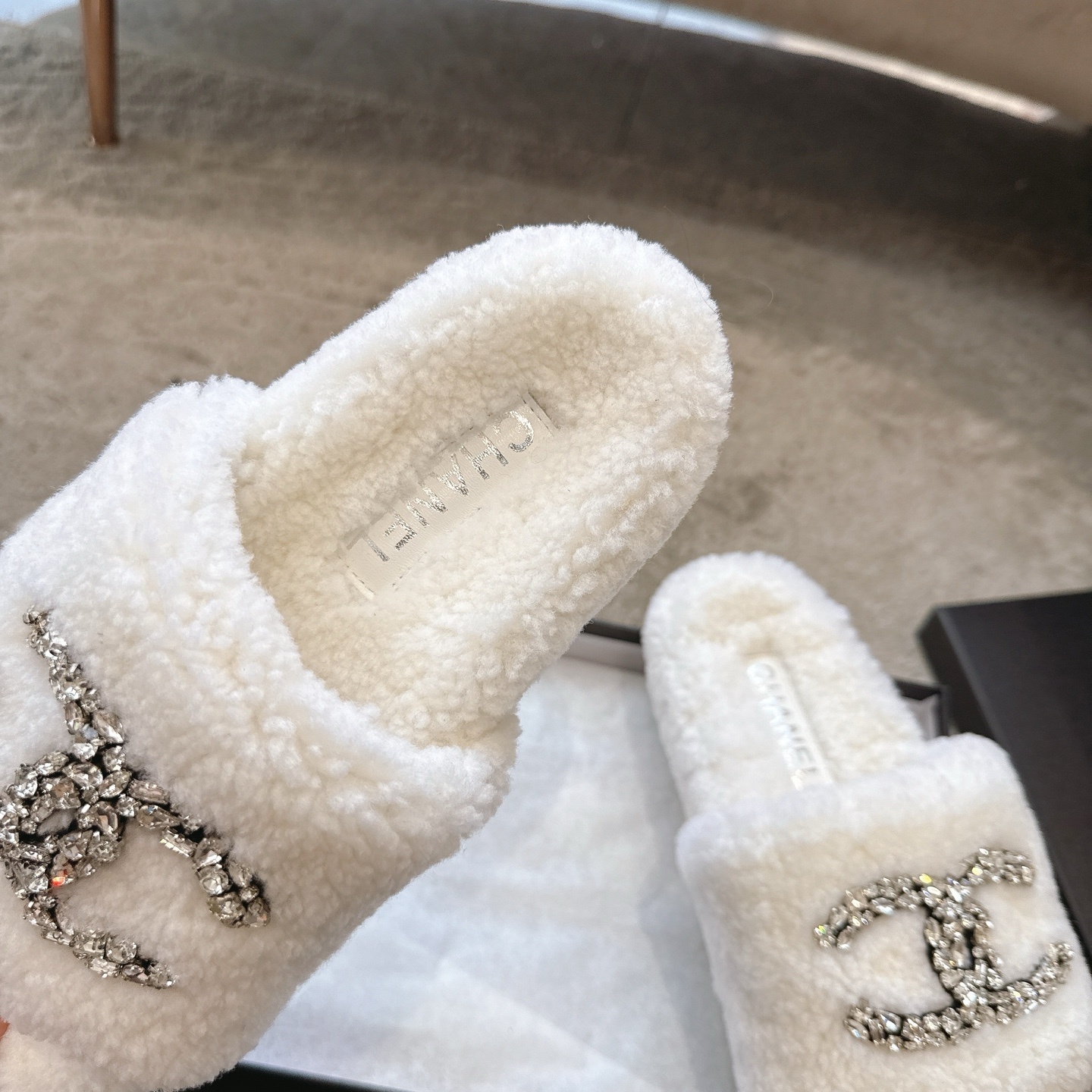 A pair of luxury white Chanel shearling slides with crystal-encrusted CC logos presented in a black brand box. - Hình 8