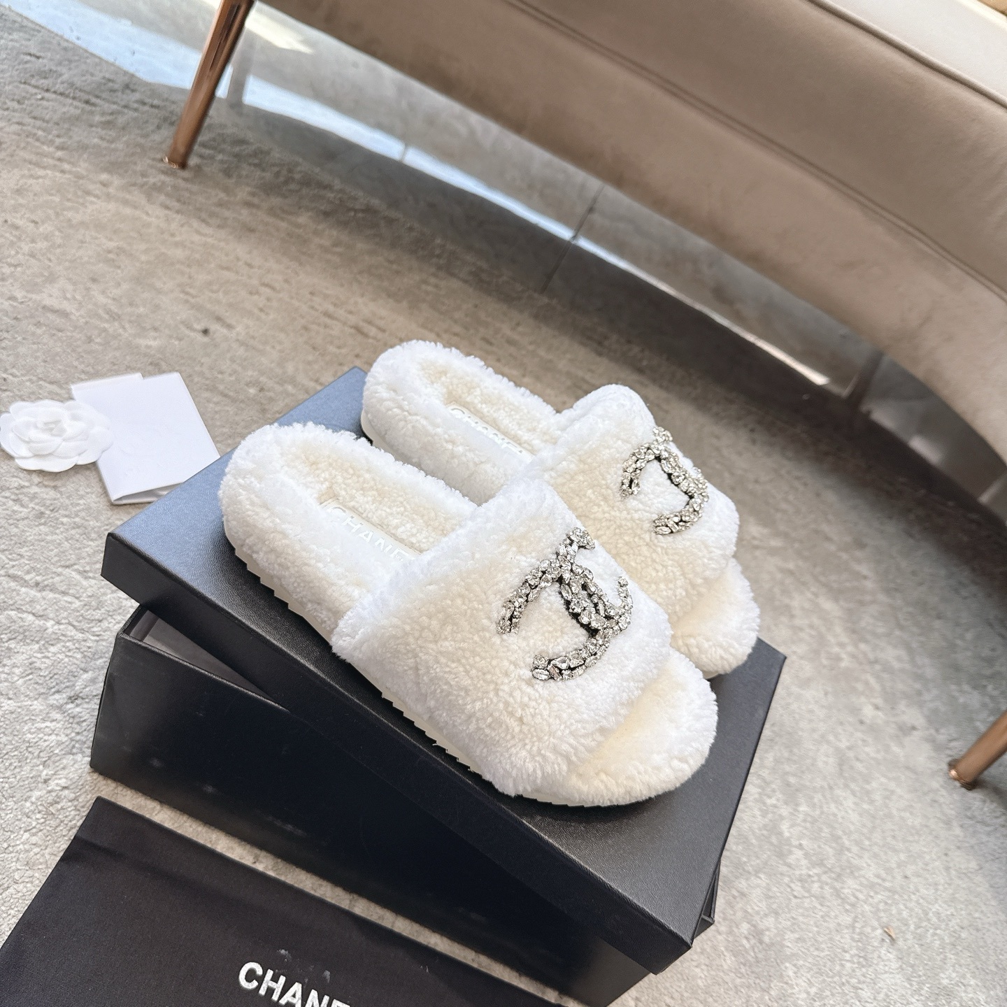A pair of luxury white Chanel shearling slides with crystal-encrusted CC logos presented in a black brand box. - Hình 6
