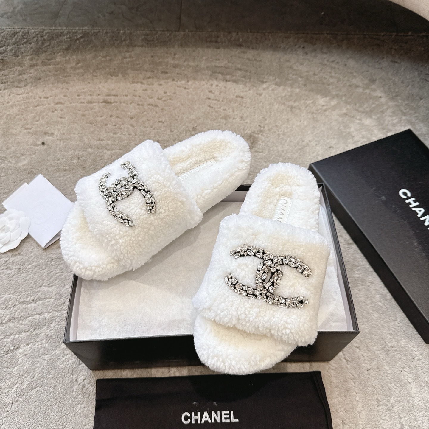A pair of luxury white Chanel shearling slides with crystal-encrusted CC logos presented in a black brand box. - Hình 5