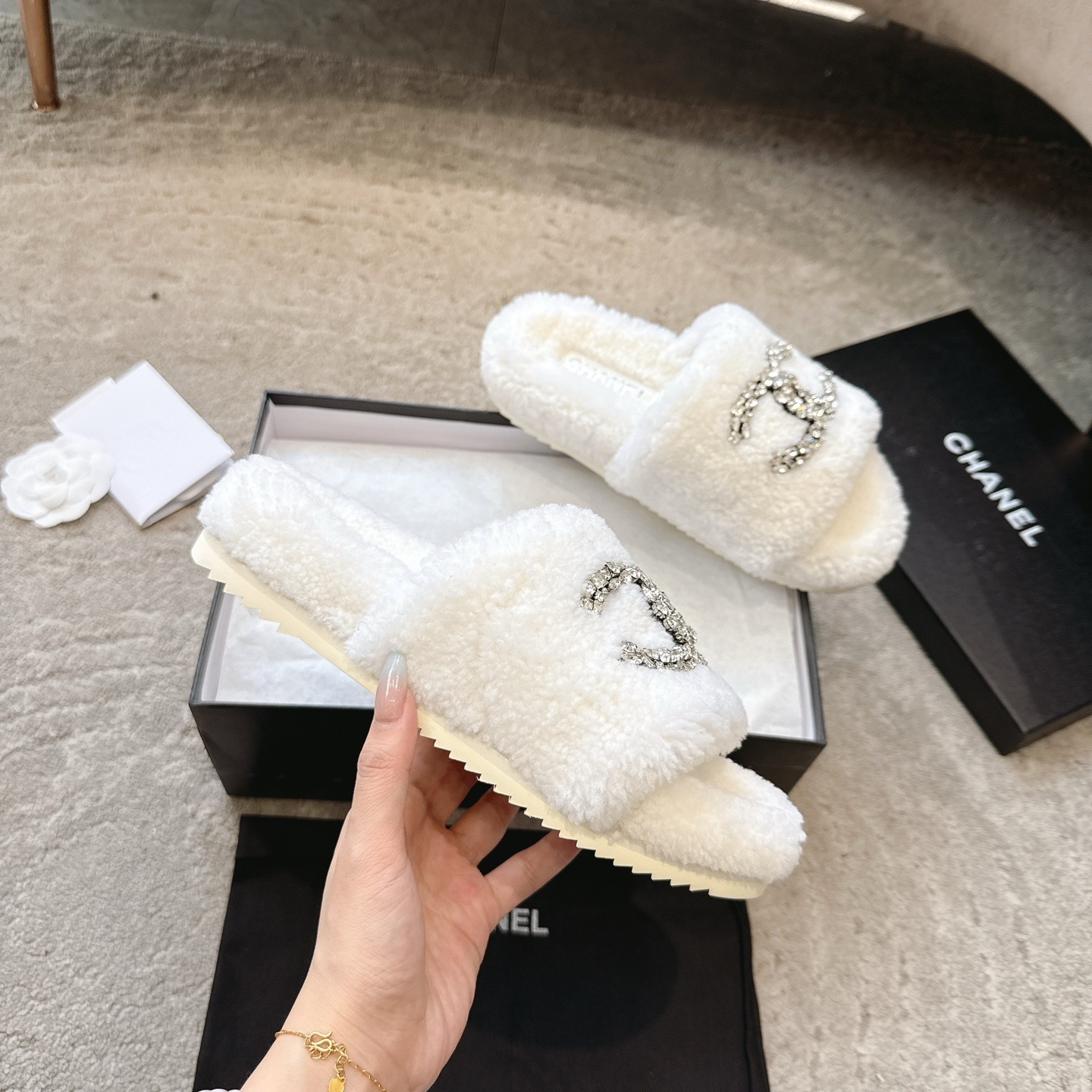 A pair of luxury white Chanel shearling slides with crystal-encrusted CC logos presented in a black brand box. - Hình 3