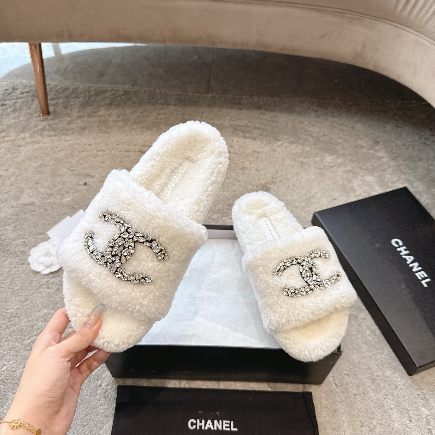 A pair of luxury white Chanel shearling slides with crystal-encrusted CC logos presented in a black brand box. - Hình 2