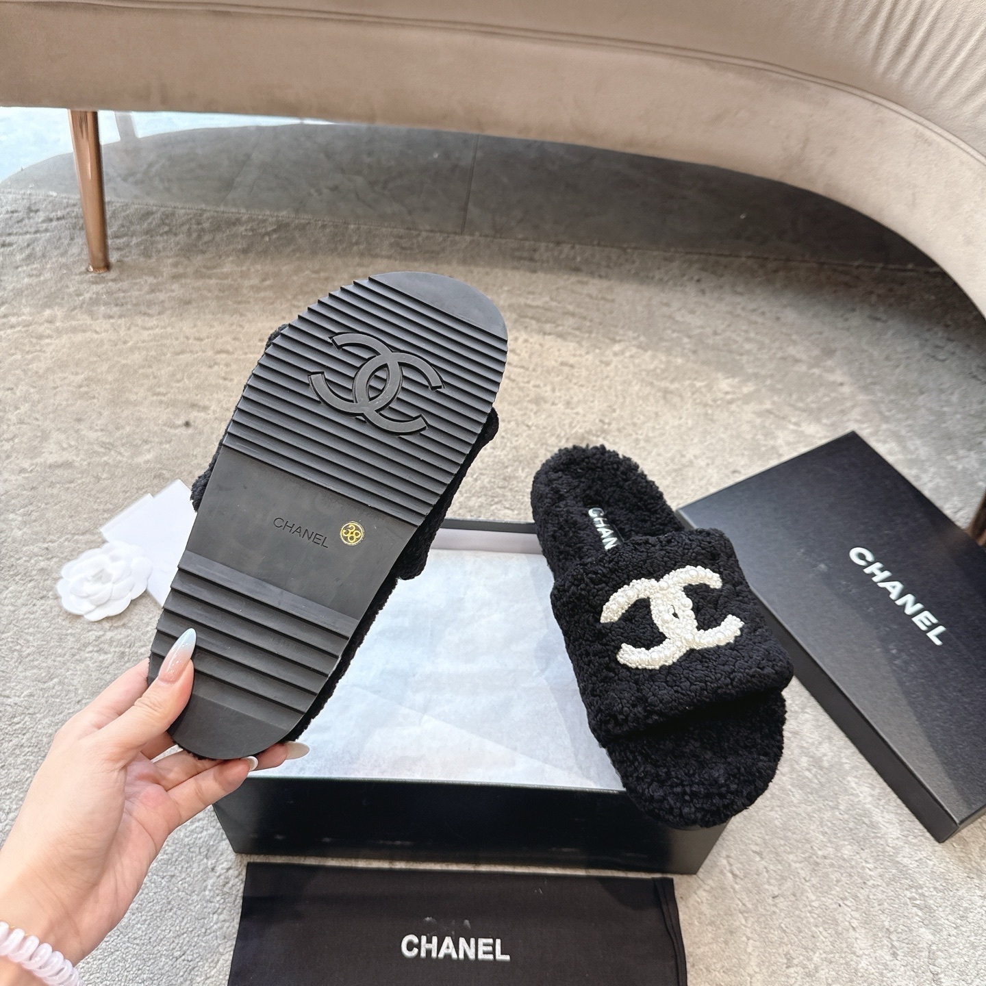 A pair of black fuzzy Chanel shearling slides with a large white pearl-embellished interlocking CC logo on the strap, shown in their original box. - Hình 9