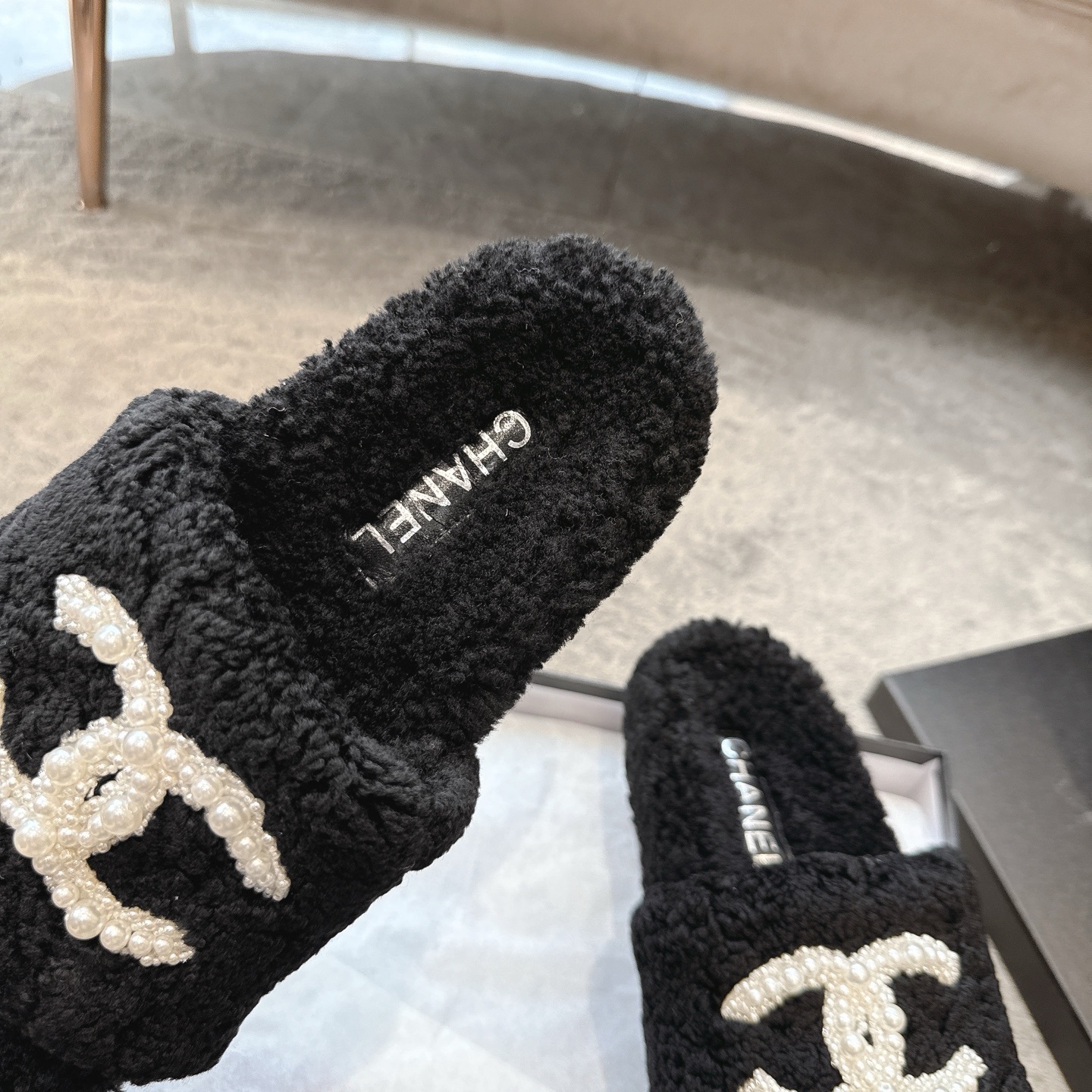 A pair of black fuzzy Chanel shearling slides with a large white pearl-embellished interlocking CC logo on the strap, shown in their original box. - Hình 8