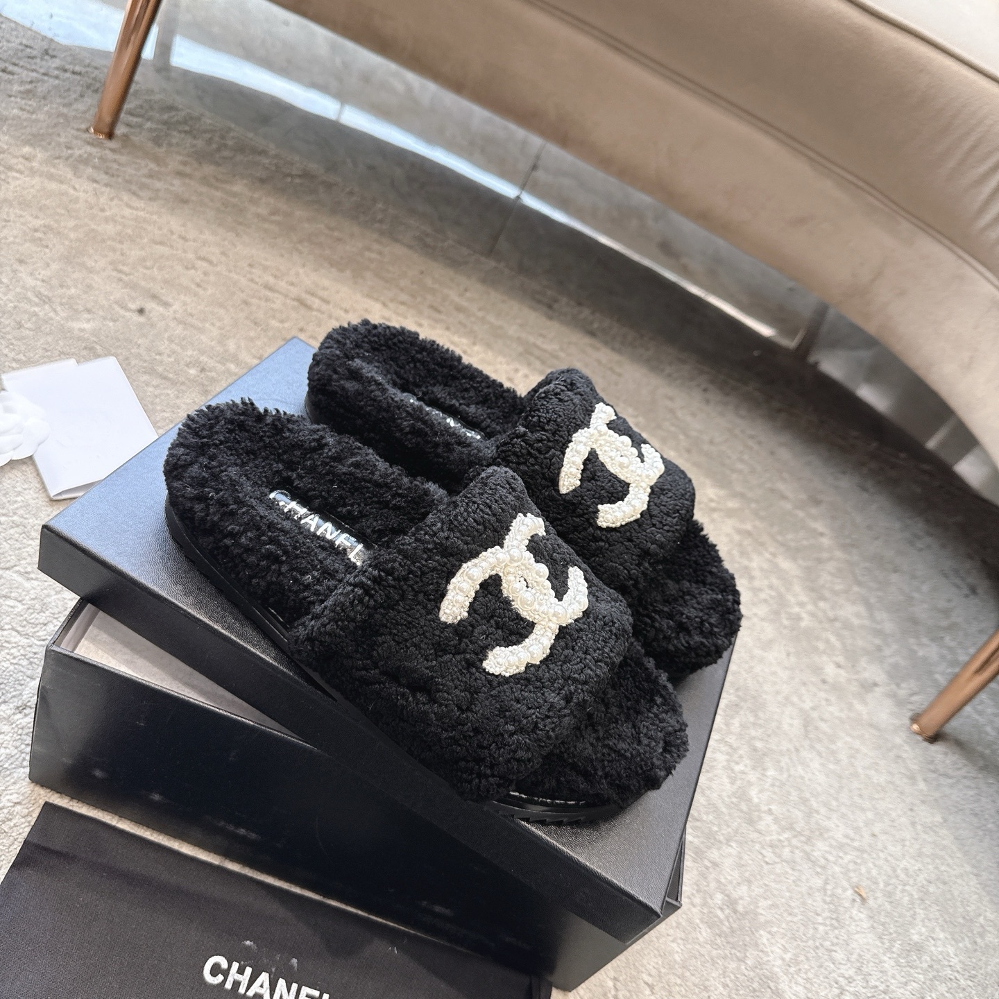 A pair of black fuzzy Chanel shearling slides with a large white pearl-embellished interlocking CC logo on the strap, shown in their original box. - Hình 6