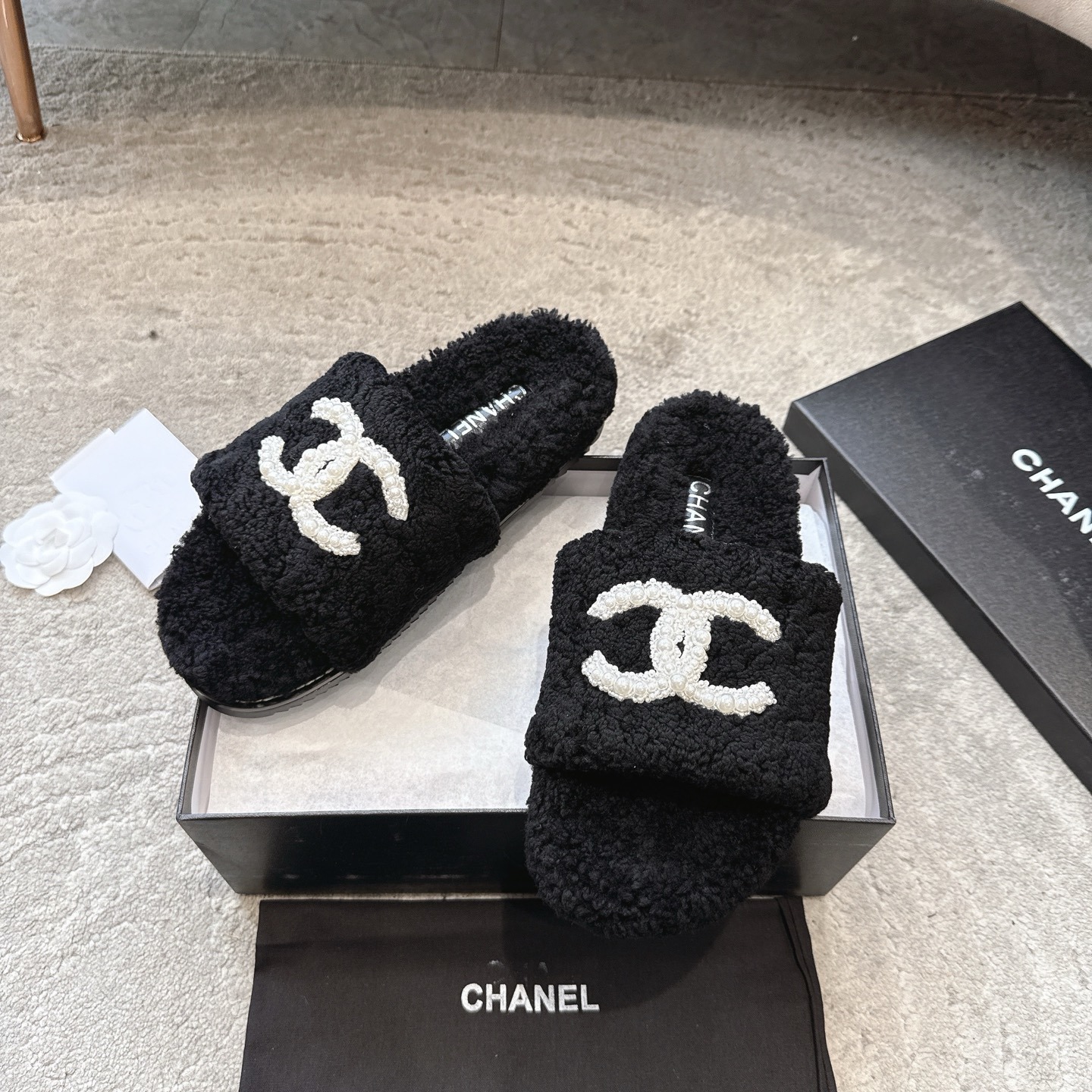 A pair of black fuzzy Chanel shearling slides with a large white pearl-embellished interlocking CC logo on the strap, shown in their original box. - Hình 5